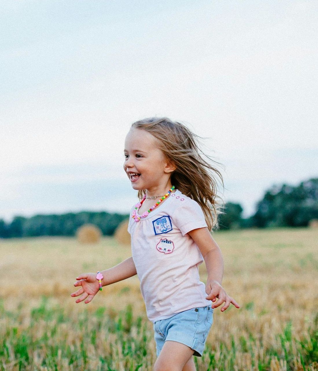 A little girl is running through a field of wheat.