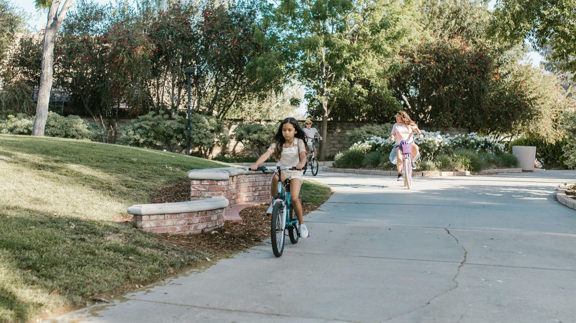 A little girl is riding a bike down a sidewalk in a park.