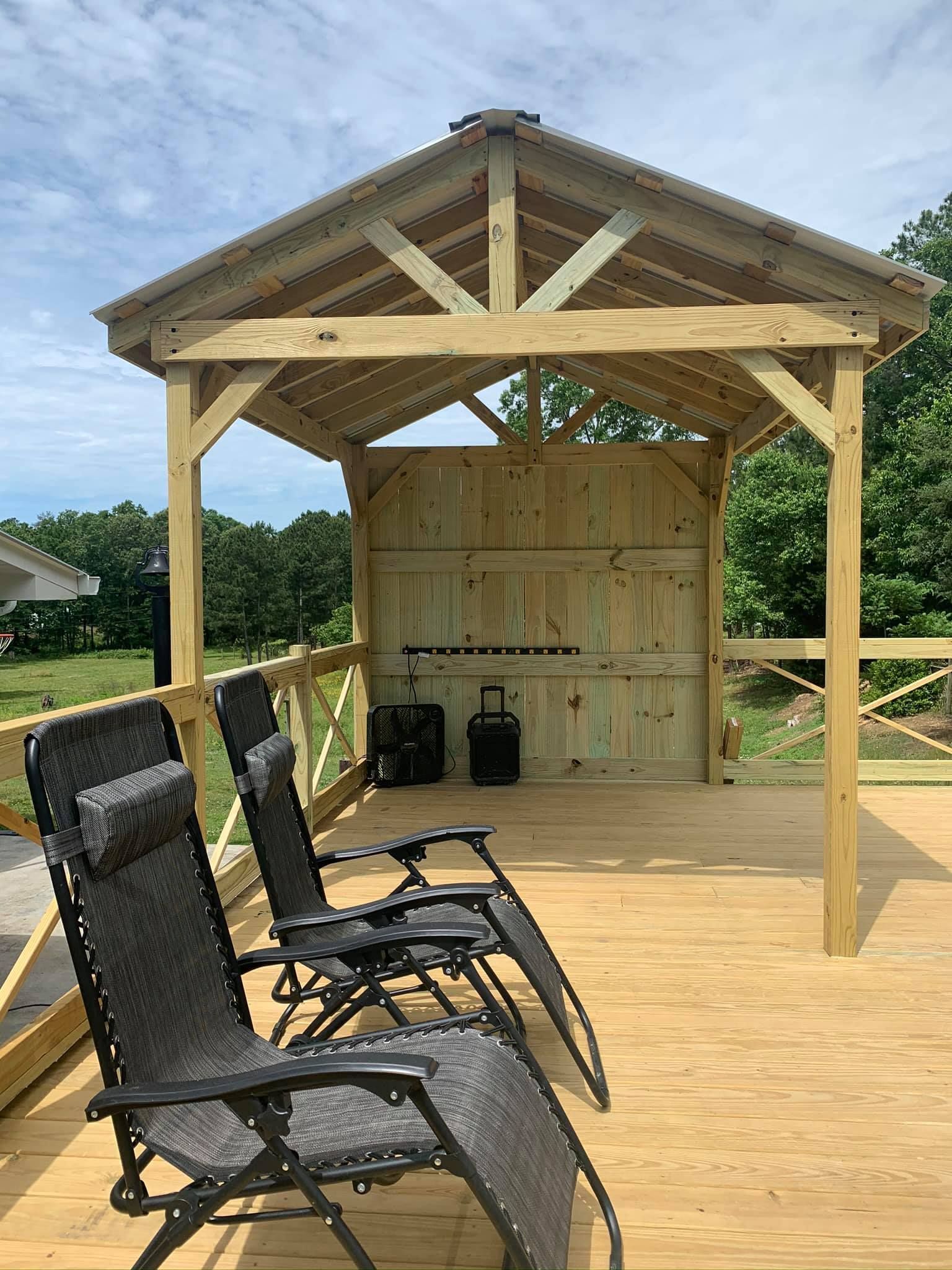 Wooden gazebo with deck, three lounge chairs, and grilling equipment.