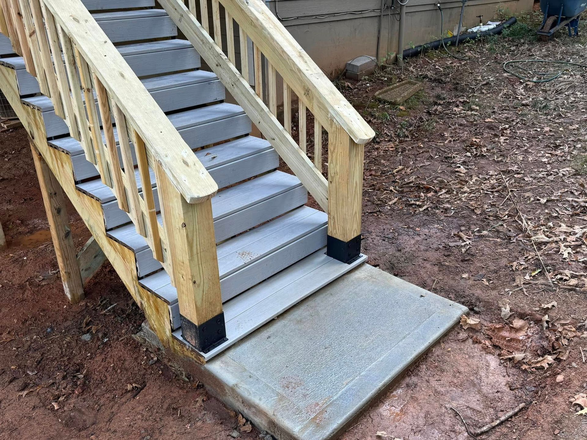 Wooden outdoor stairs with gray steps and a concrete landing on a dirt surface.
