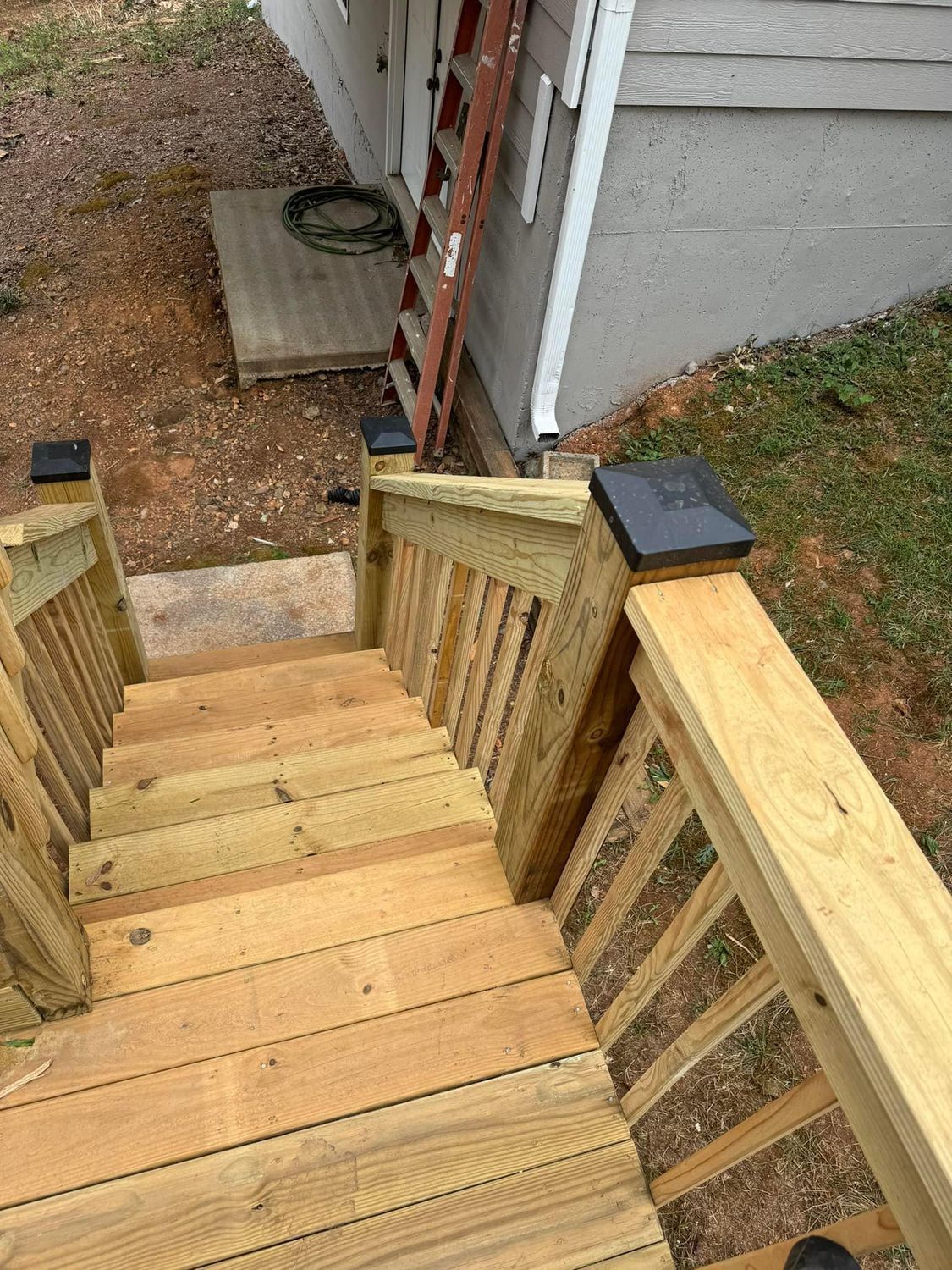 Wooden outdoor staircase with railings, brown ladder leaning against beige building.