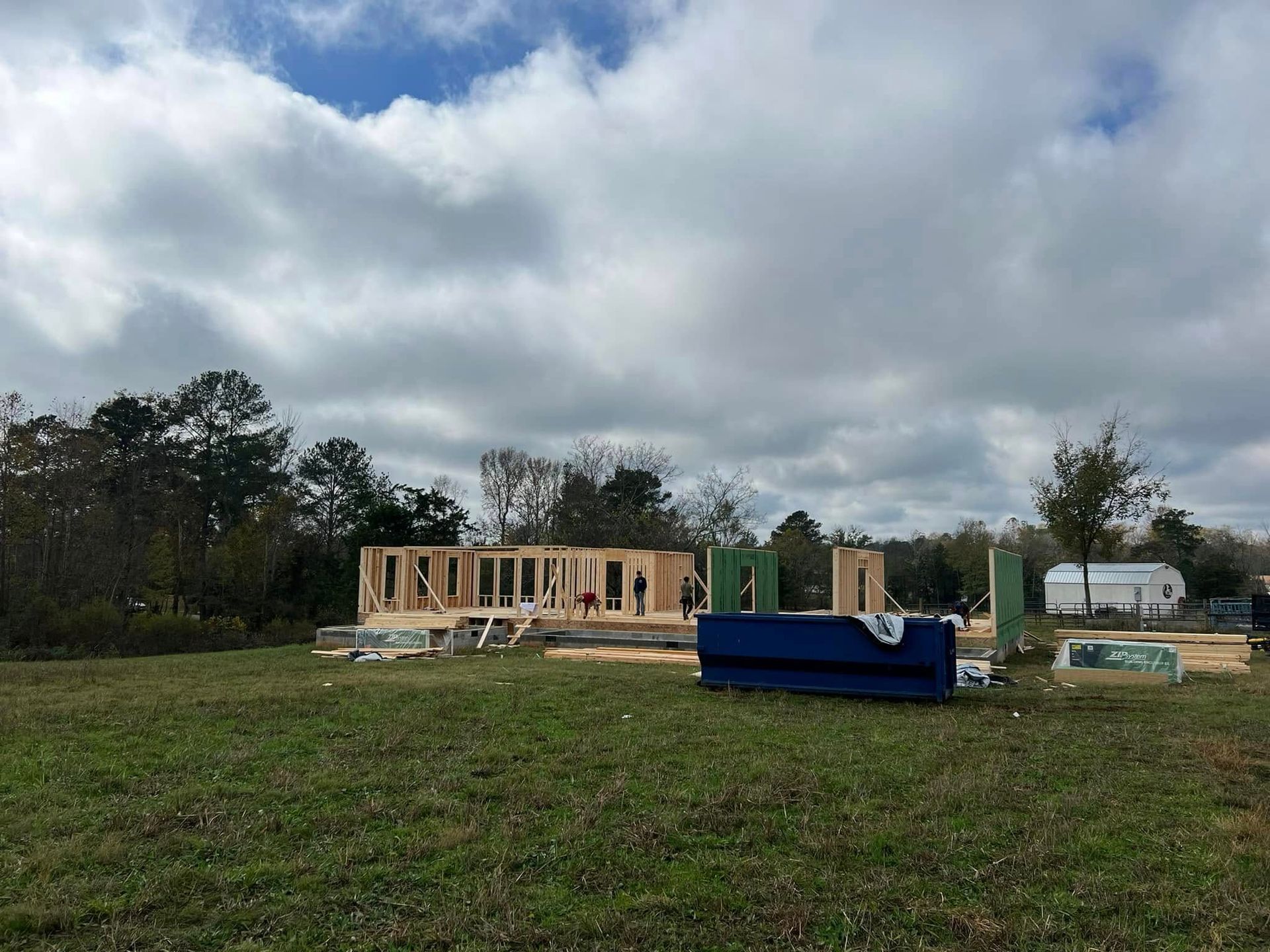Wooden frame of a house under construction on a grassy lot, with a cloudy sky.