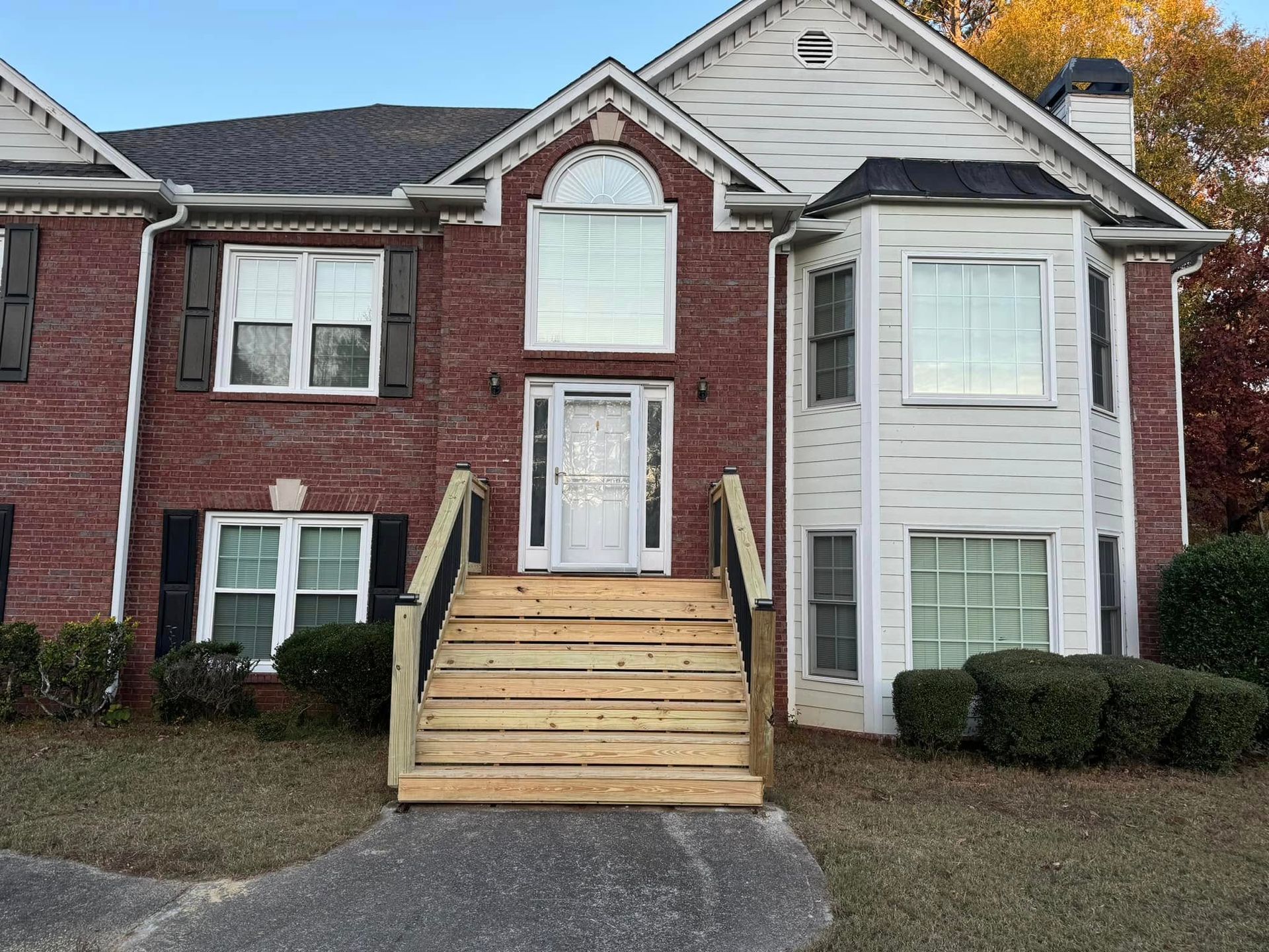 Brick and white house with wooden steps leading to the front door; shrubs are in front.