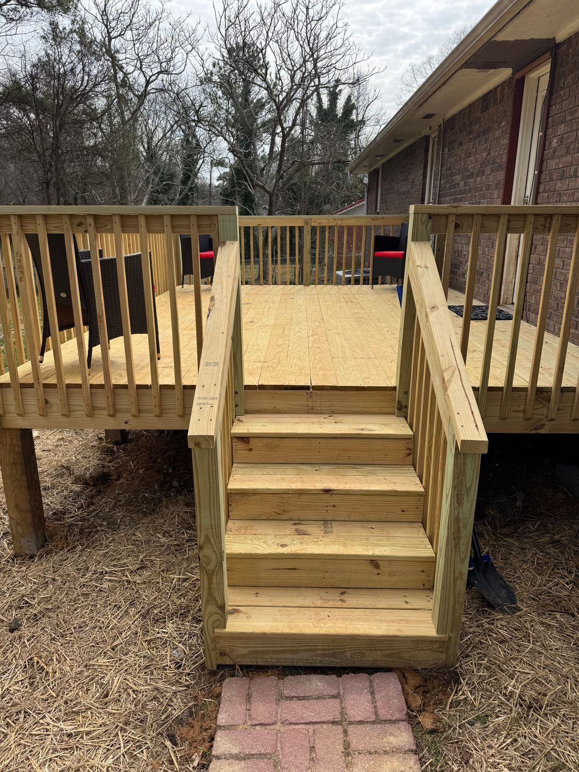 Wooden deck with stairs leading to a brick pathway. The deck is attached to a brick house, and the setting appears to be outdoors.