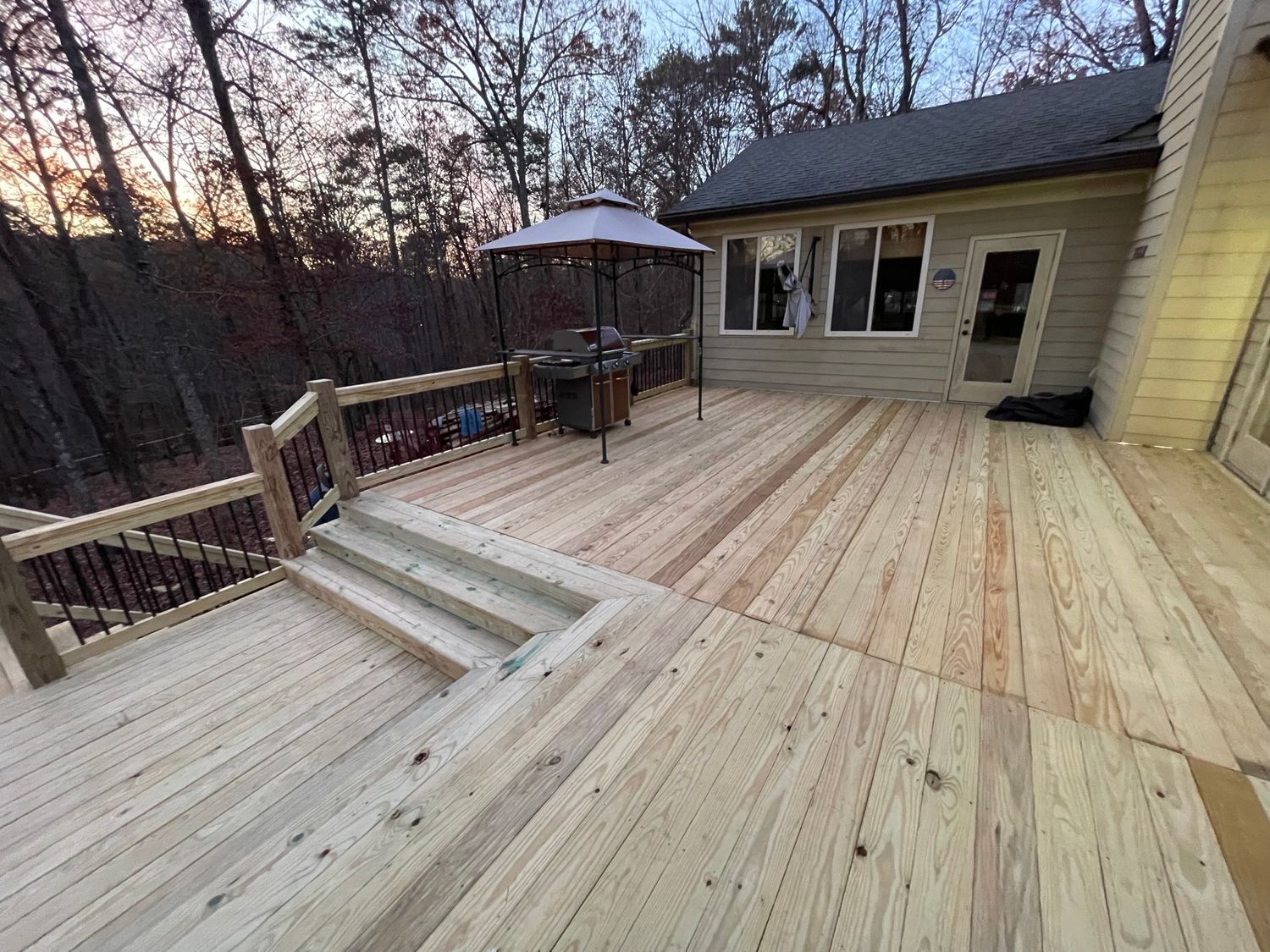 Wooden deck with steps, railing, and an umbrella, extending from a house. Dusk setting.