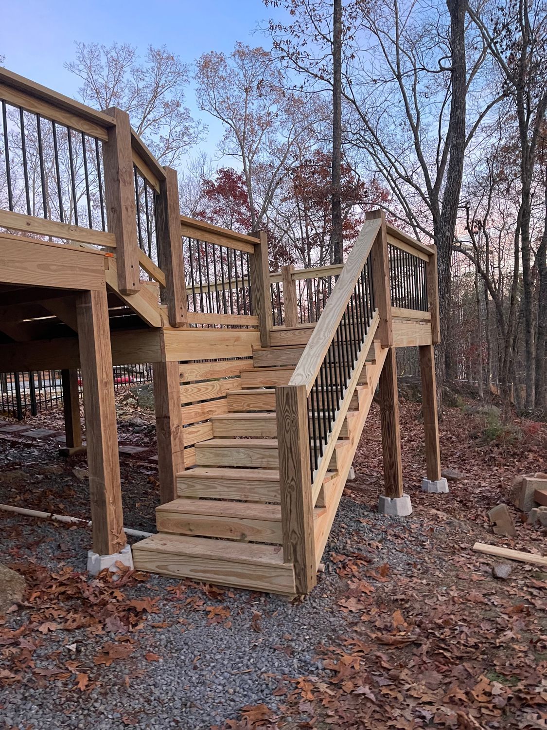 Wooden deck and stairs with black railing in a wooded setting.