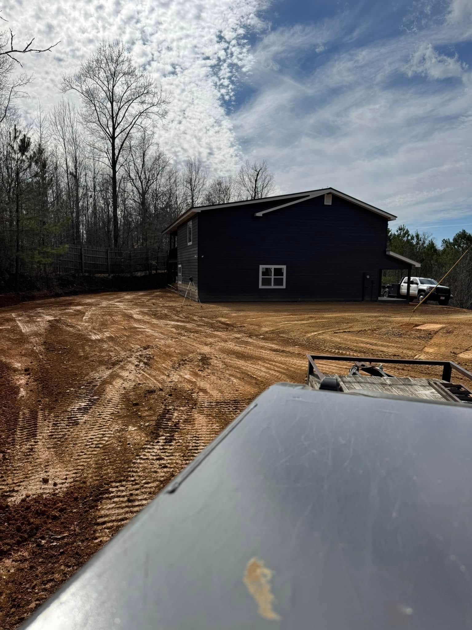 Dark house with a white window and a dirt yard in front of it. Trees and cloudy sky in the background.