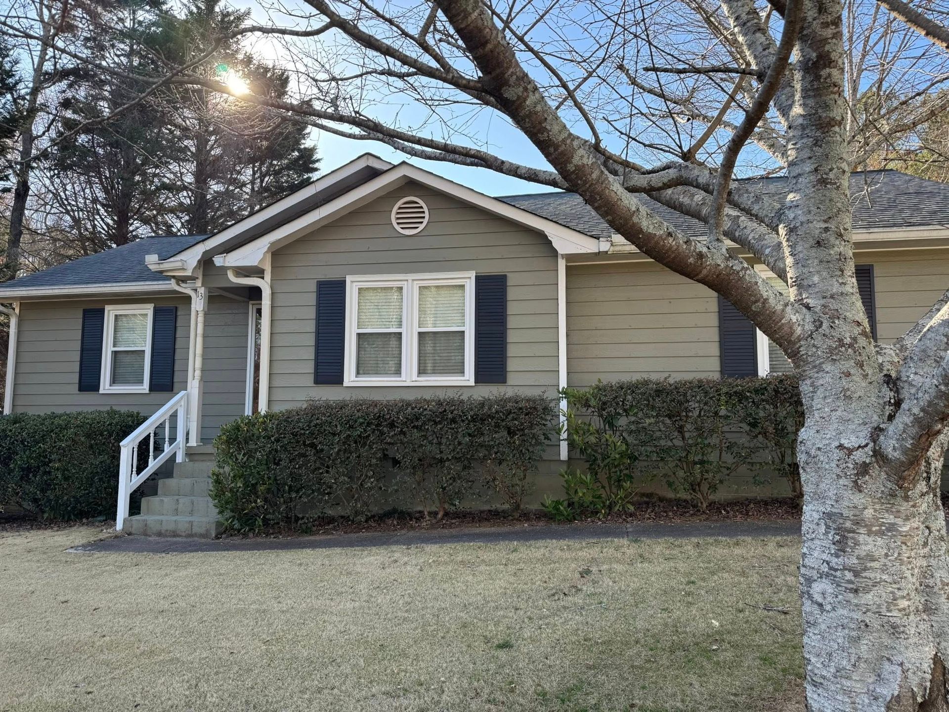 Tan house with blue shutters, a small front porch, and a tree in the foreground.