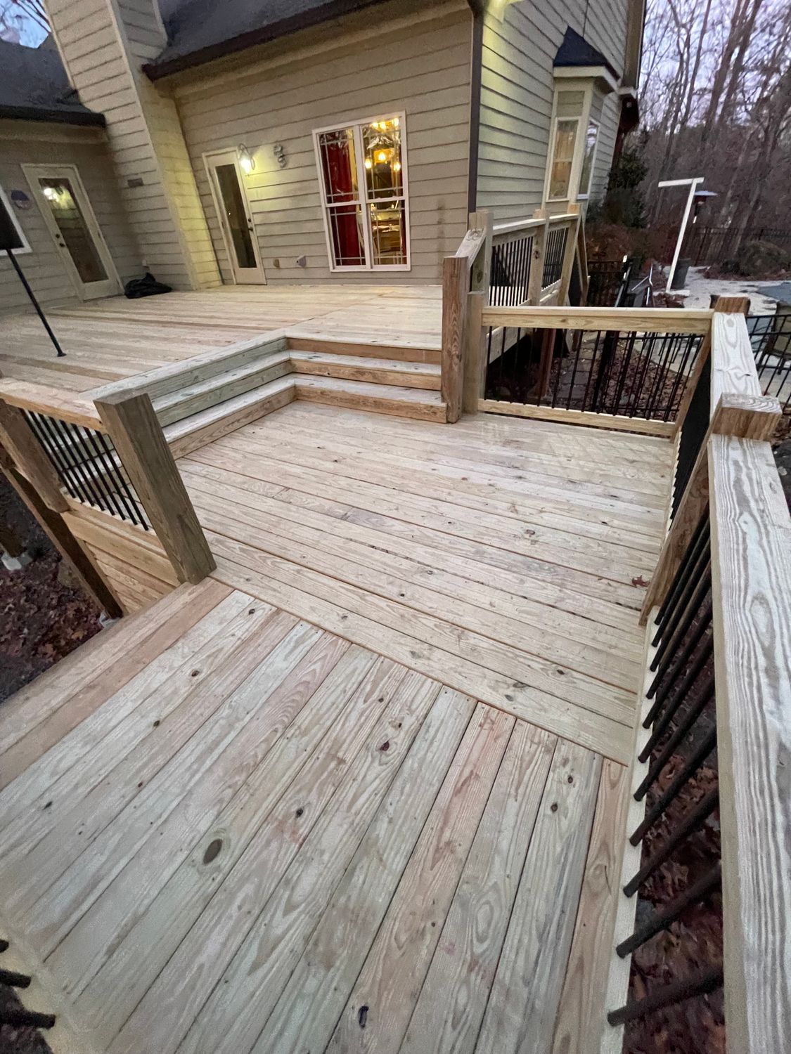 Wooden deck with railings and steps, leading to a house with large windows.