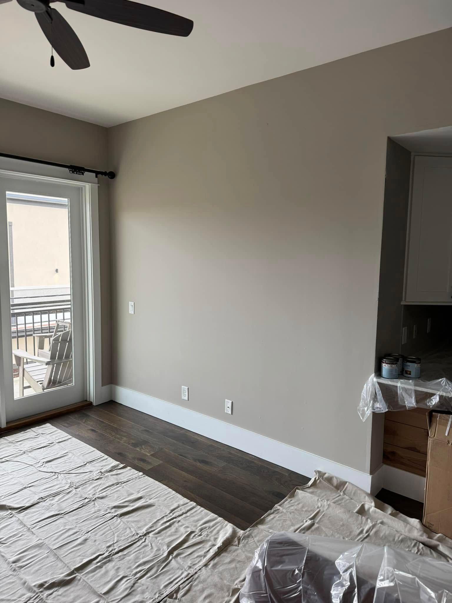 Room with a beige wall, dark wood floor, a balcony door with white curtains, and a partially covered countertop.