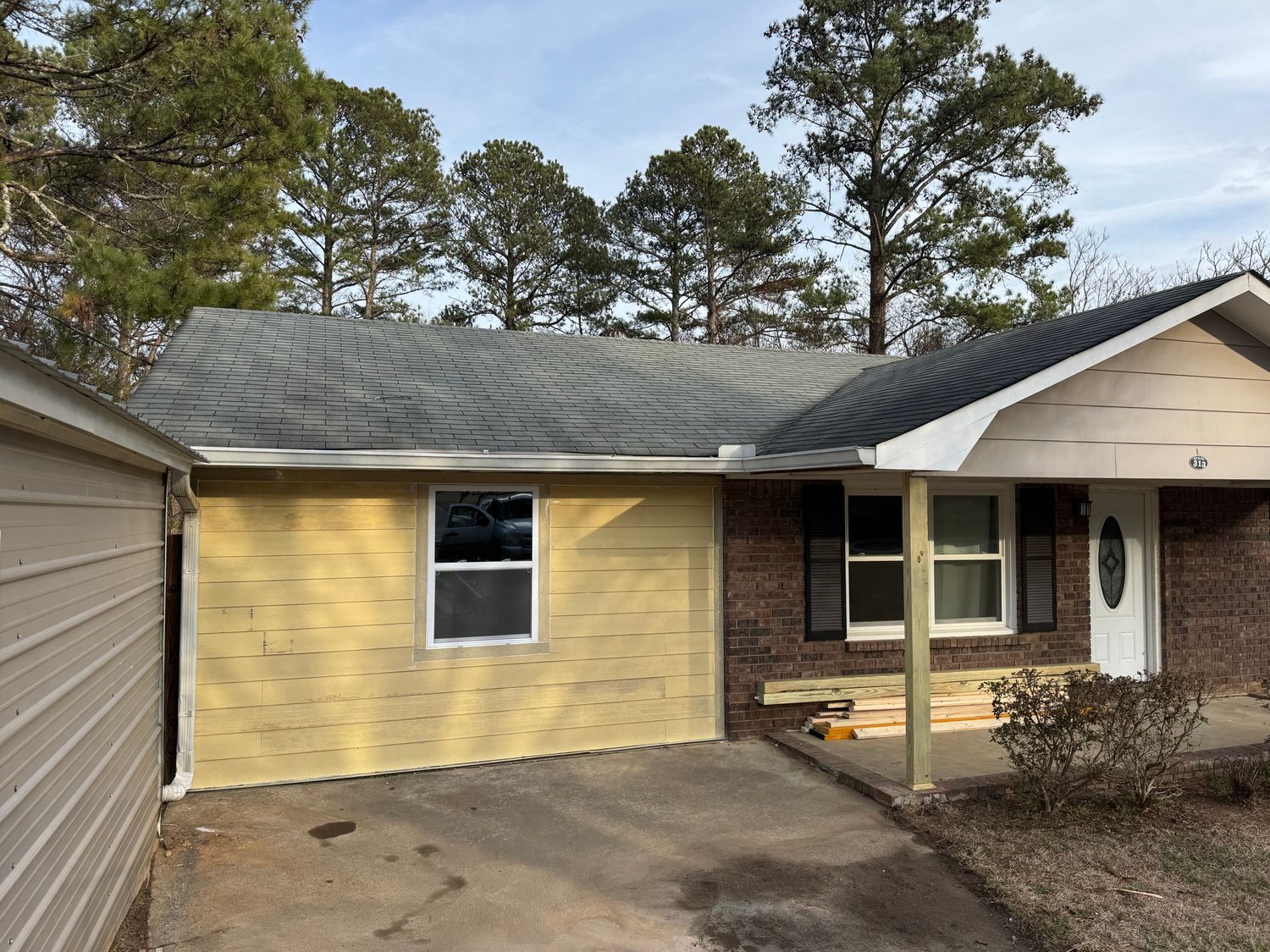 Yellow-sided house with dark roof and brick facade; driveway in foreground.