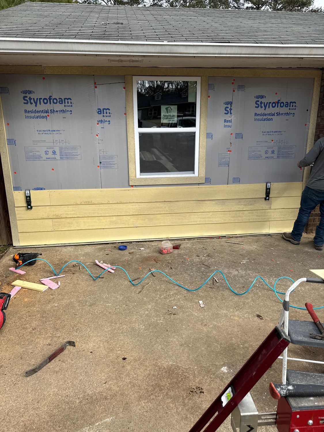 Construction in progress: Exterior wall with insulation, new window, and partial siding. Person installs siding.