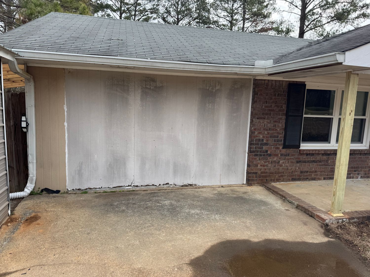 Exterior house wall with weathered siding, next to a brick section and a covered porch.