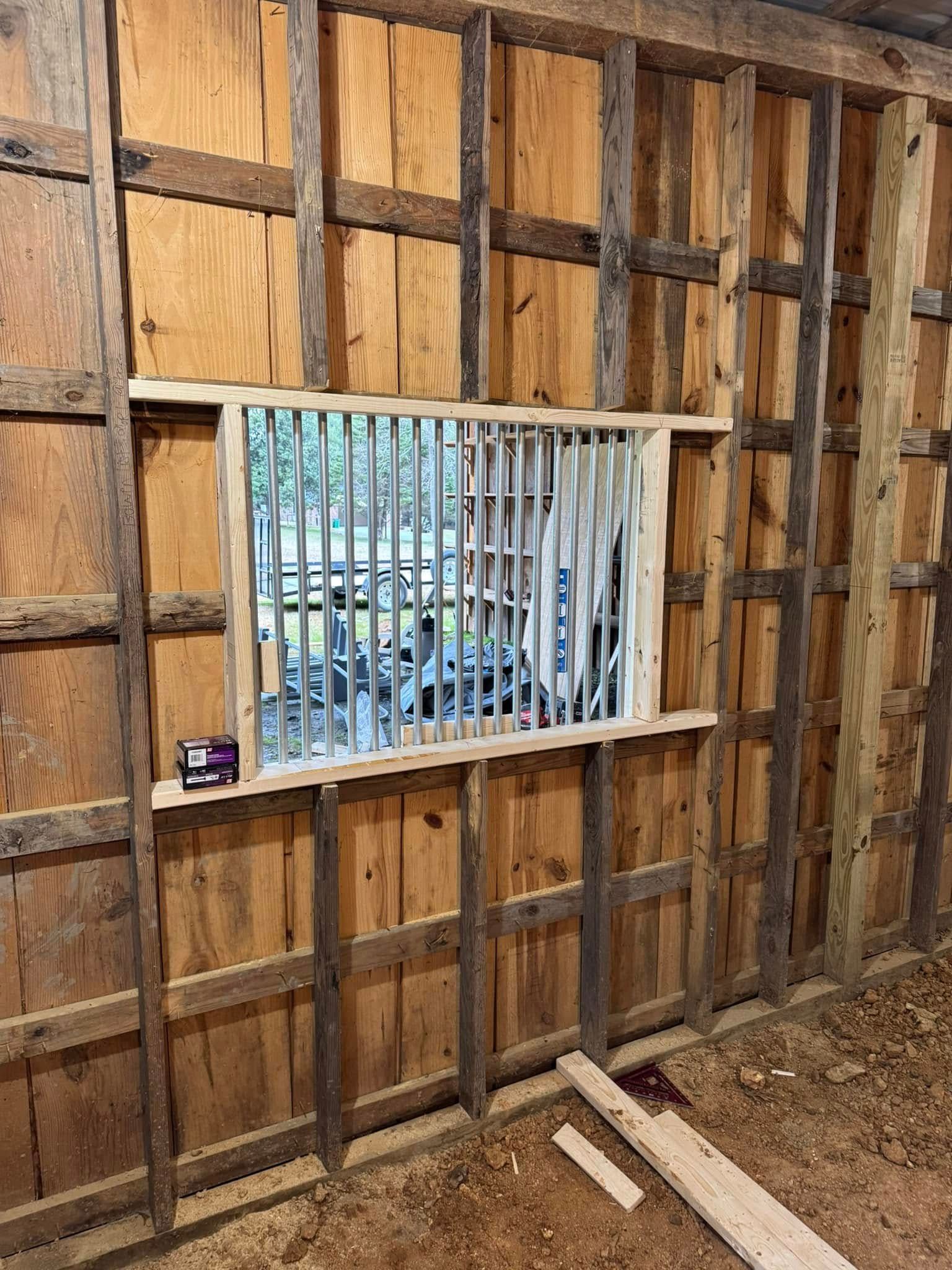 Interior wall with framed window and vertical wooden bars. Unfinished construction with visible wooden beams.