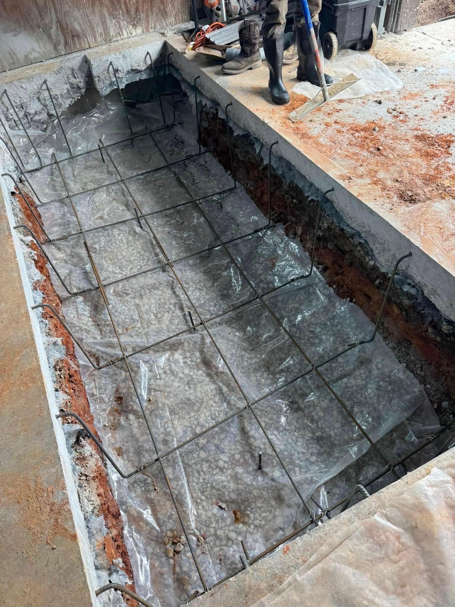 Construction site: Rectangular concrete form with rebar grid and plastic sheeting; workers in background.