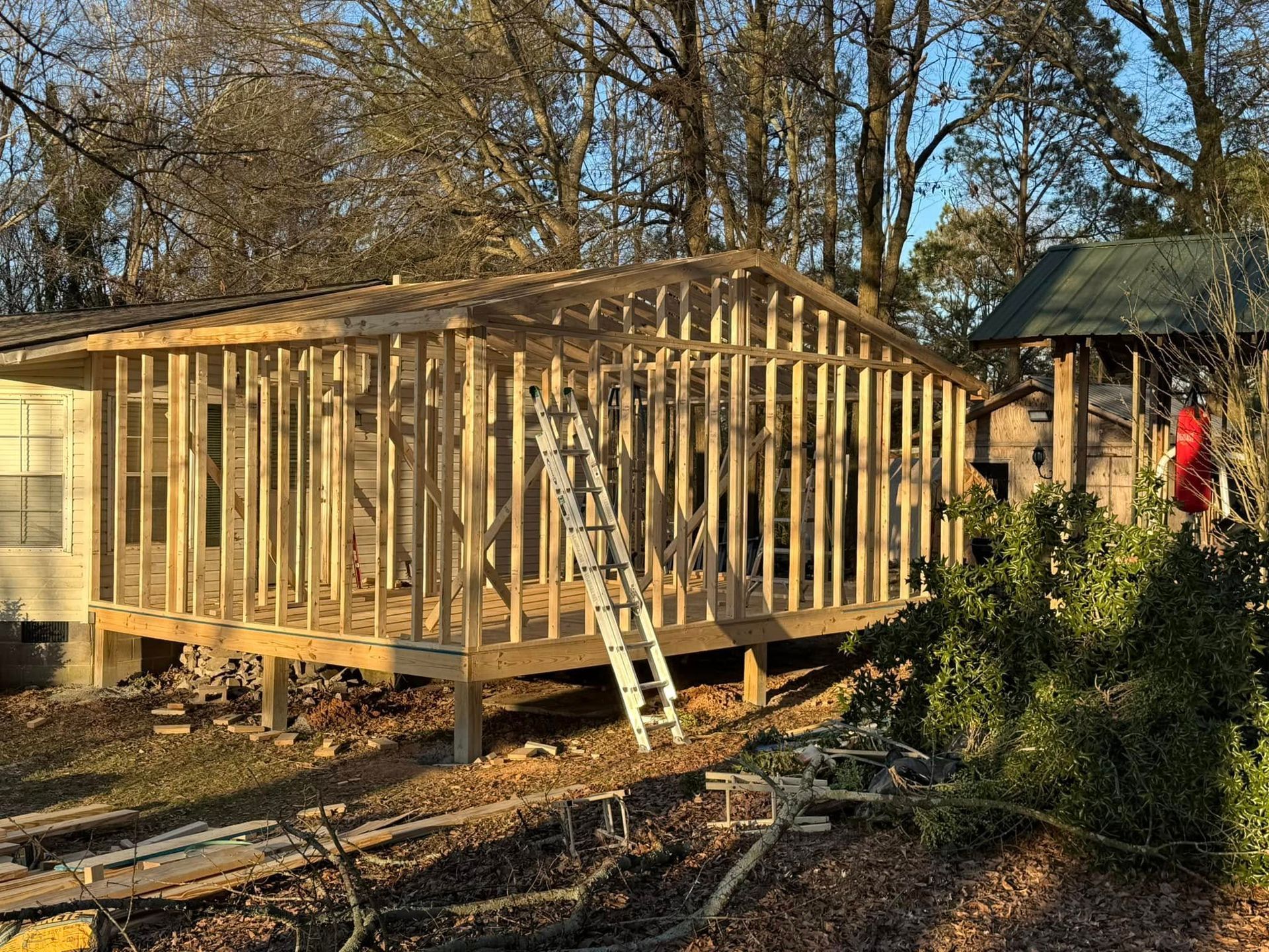 Framing of a wooden addition to a house; includes a ladder and debris.