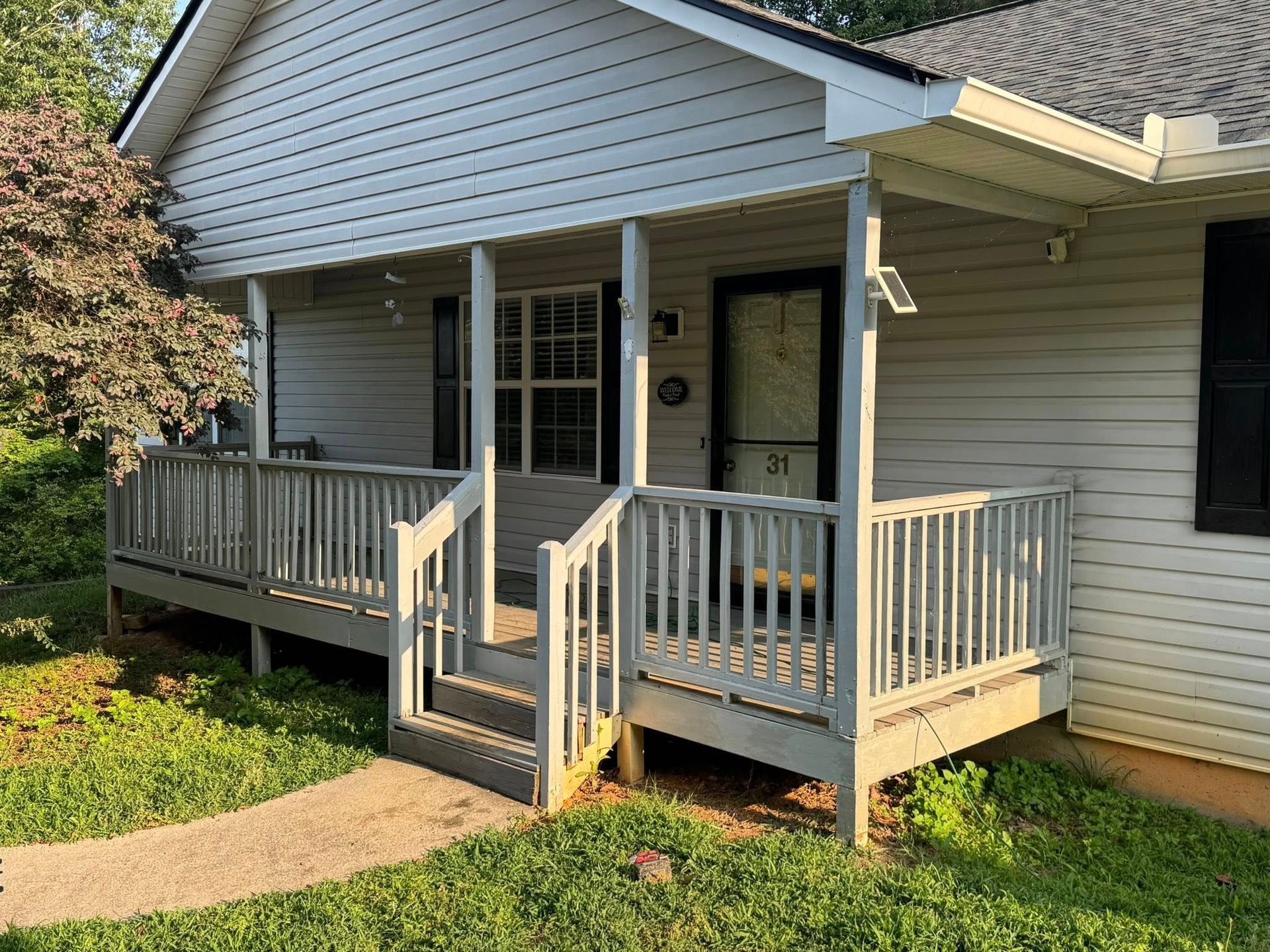 Front of a house with a porch and steps, number 71 on the door, gray siding and trim, green grass.