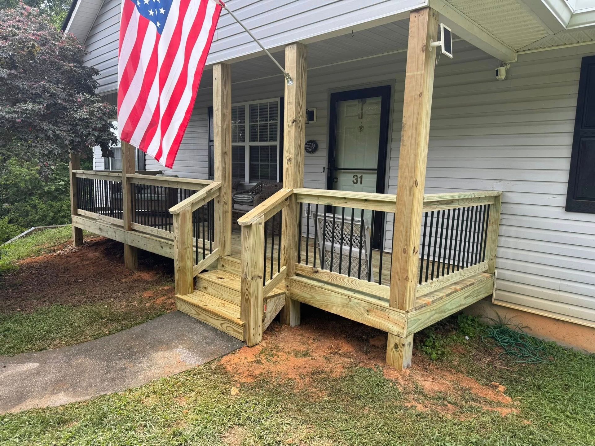 Newly built wooden porch with steps, black railing, American flag, and house number 21.