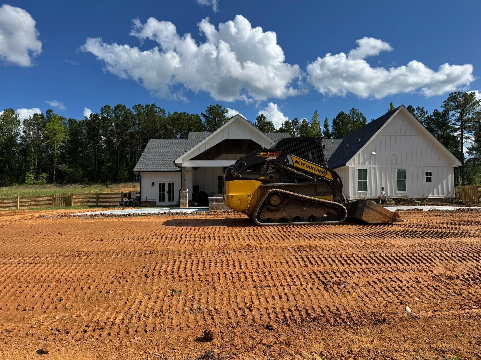 Yellow skid steer on construction site in front of a white house with a dark roof.