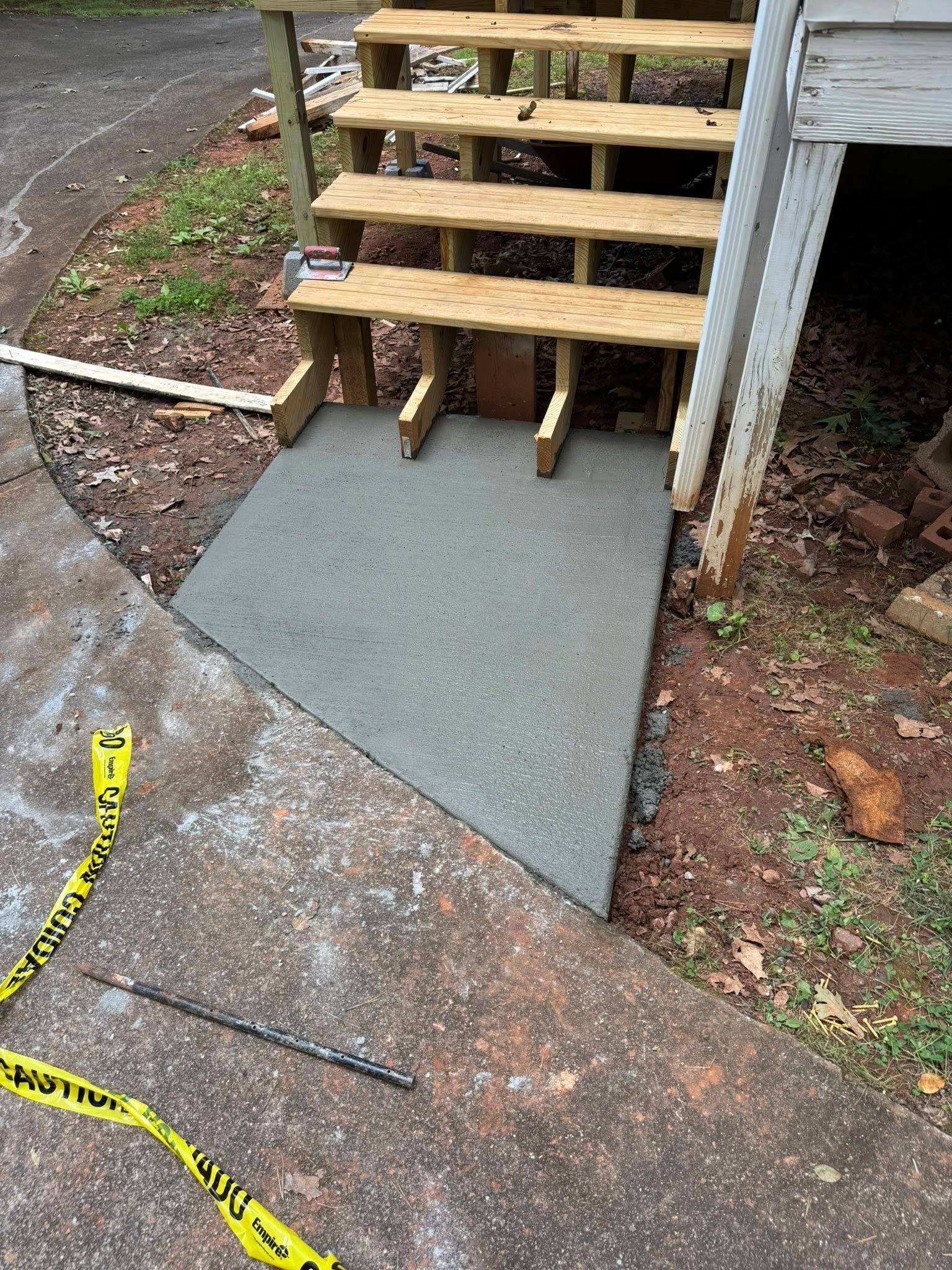 Concrete ramp leading to wooden stairs, constructed near a house. Yellow caution tape is present.