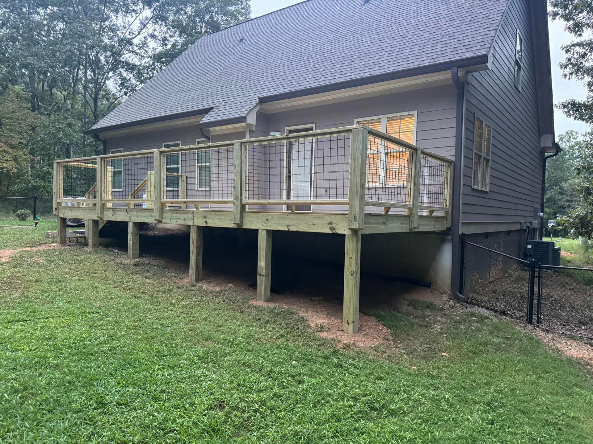 A wooden deck extends from a gray house with a metal roof, set on a grassy hill.