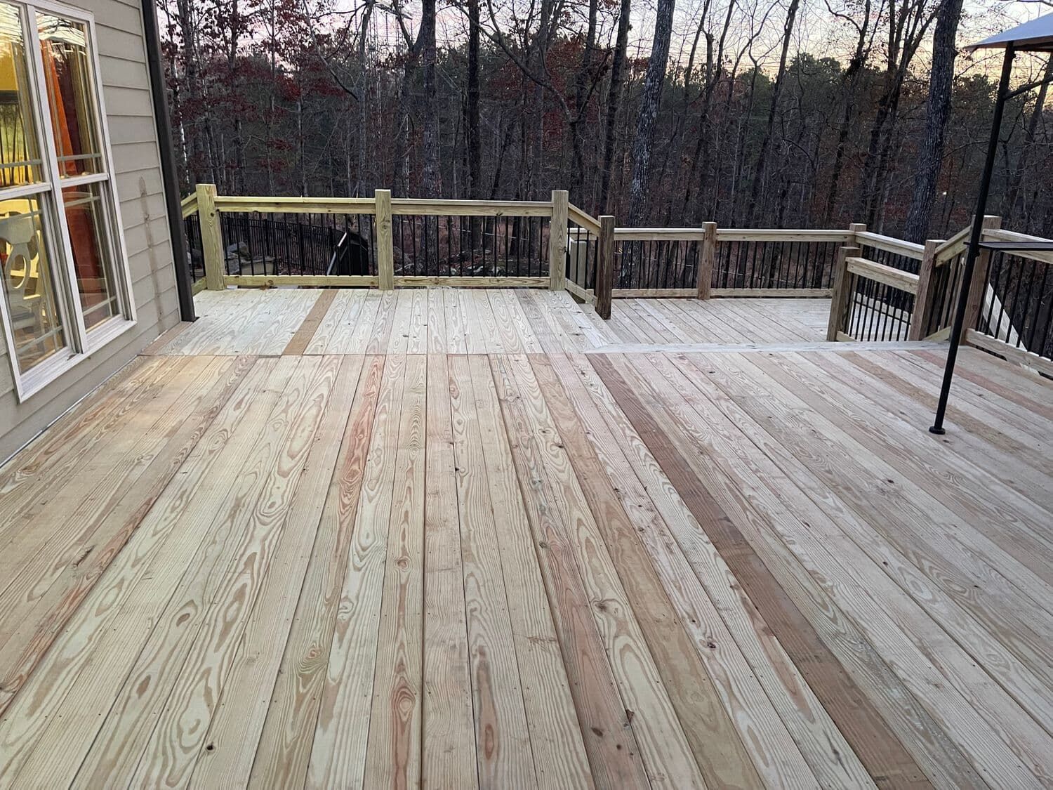 Wooden deck with railings, overlooking a wooded area. The deck is light-colored and empty.