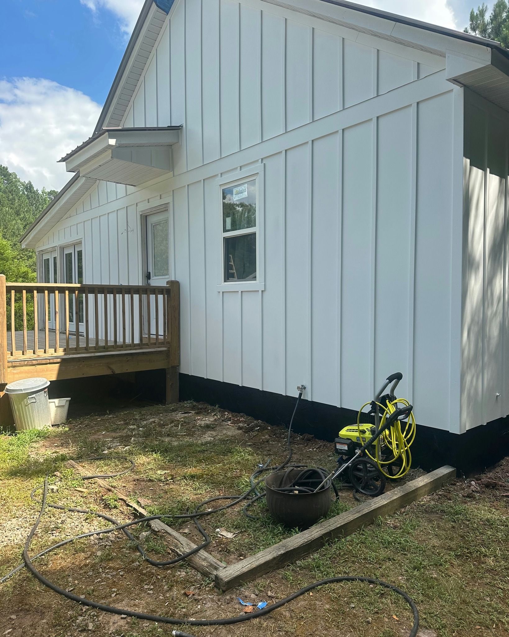 White farmhouse with vertical siding and small wooden deck. Green lawn mower sits near foundation.