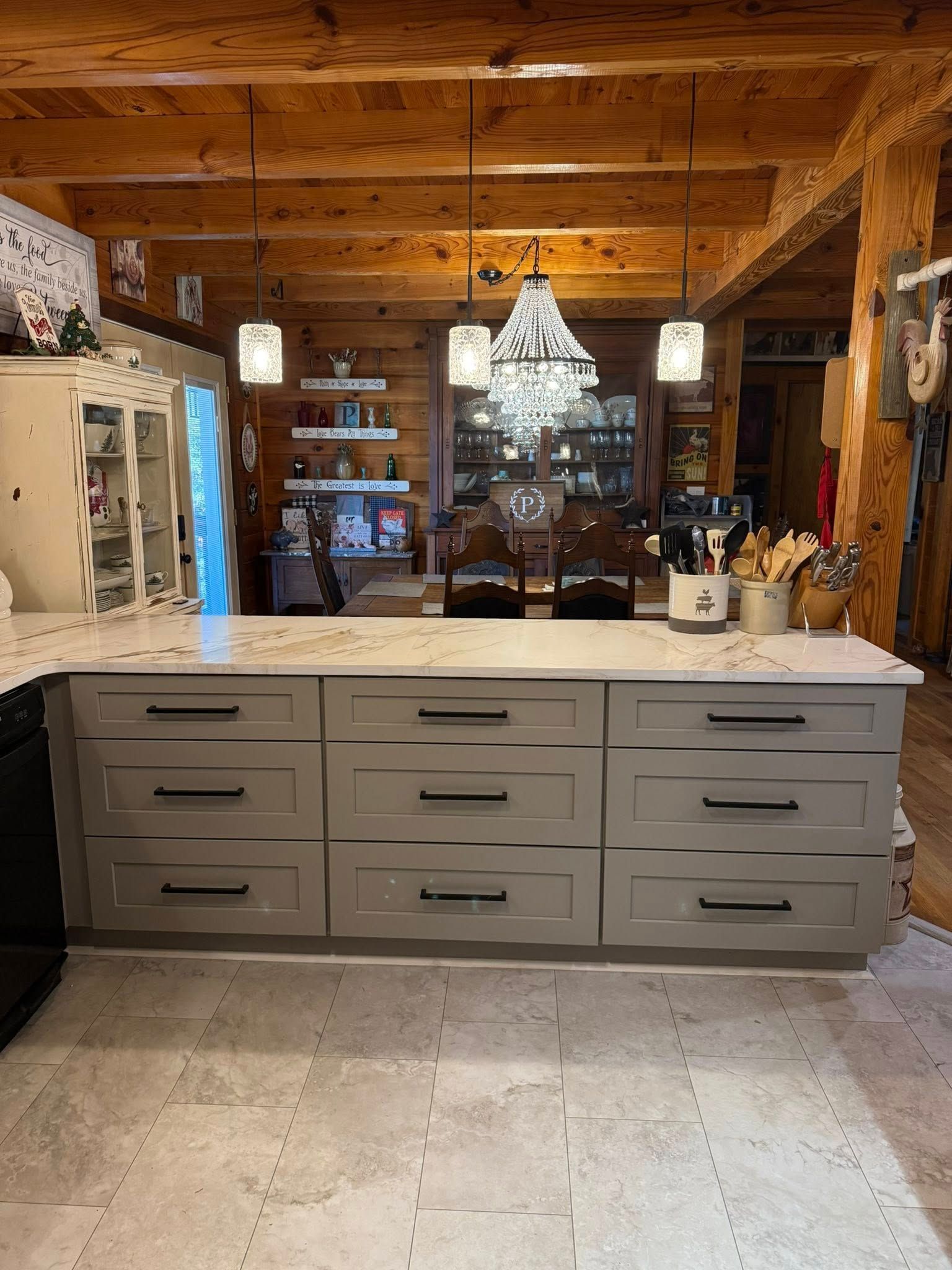 Kitchen island with gray cabinets, white countertop, and a chandelier, set in a rustic room with wooden beams and shelves.