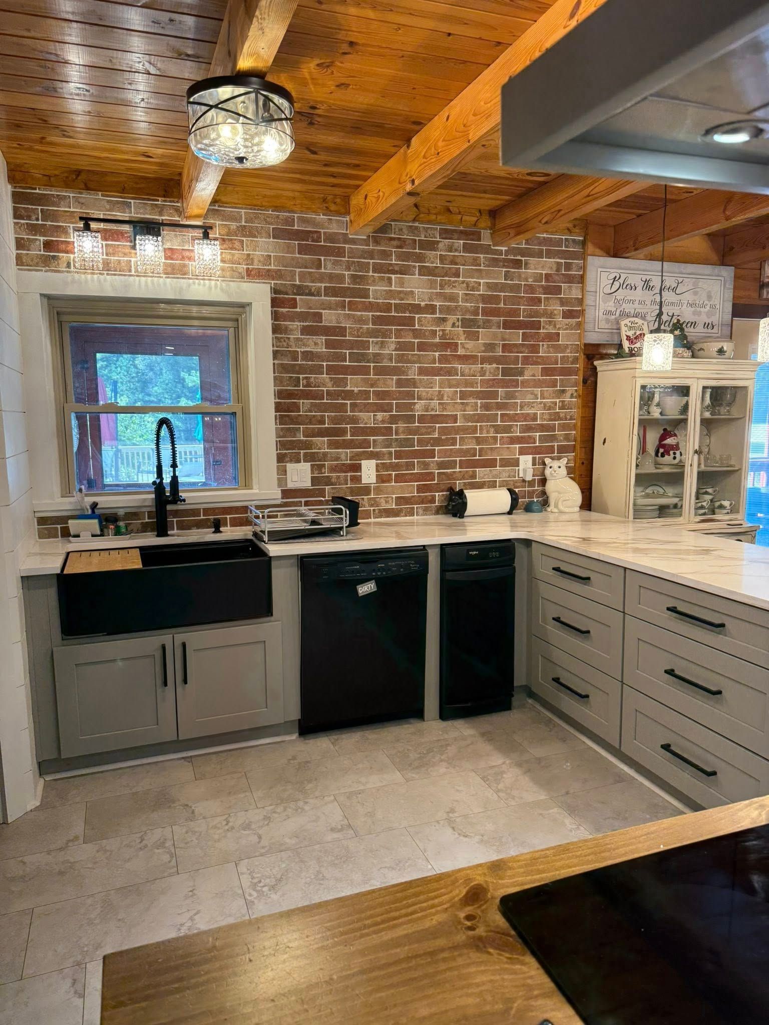 Kitchen with exposed brick wall, gray cabinets, black sink and appliances, and wood ceiling.