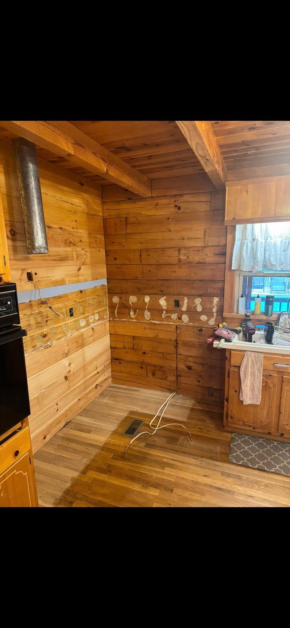 Wooden interior of a kitchen with light-colored wooden walls and cabinets. A range and sink are visible.