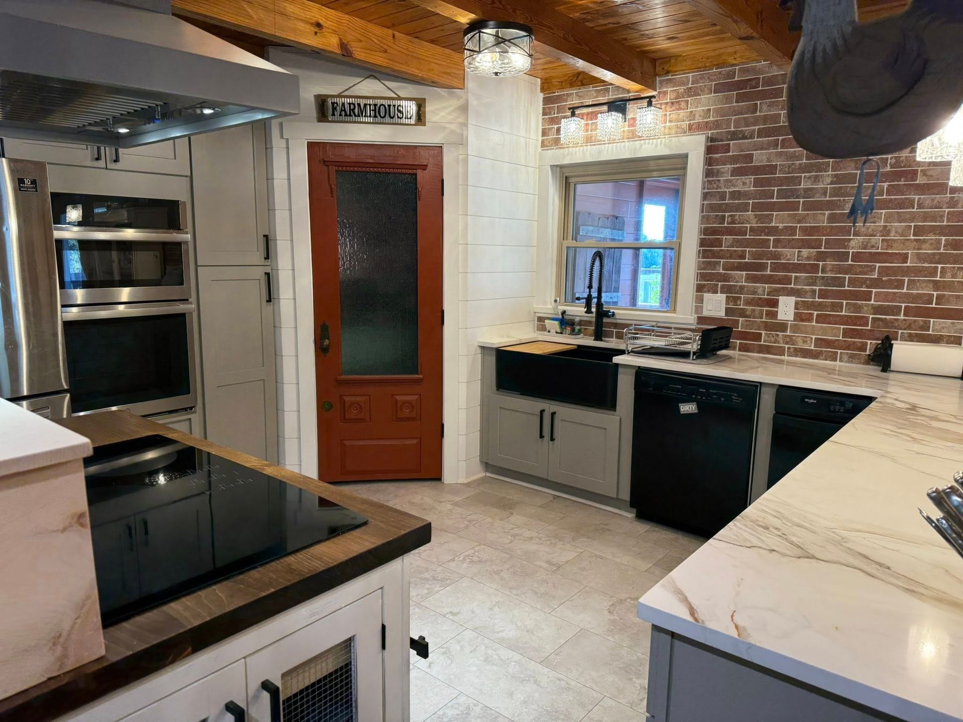Kitchen with exposed brick, stainless steel appliances, red door, and marble countertops.