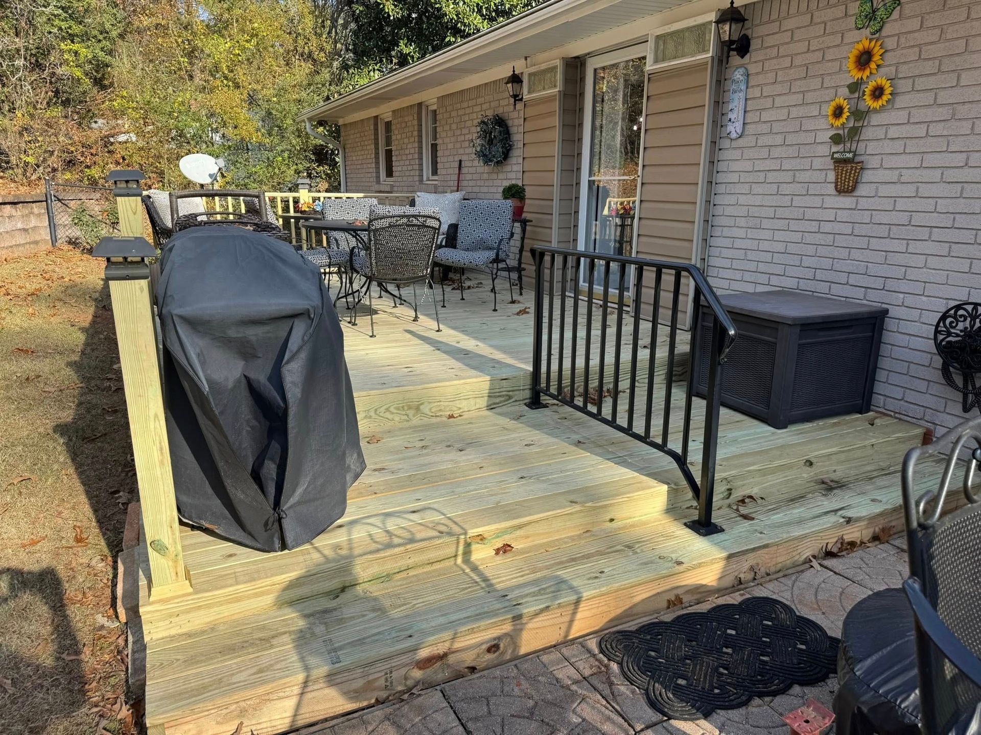 Wooden deck with steps, black railing, grill, and patio furniture next to a brick building.