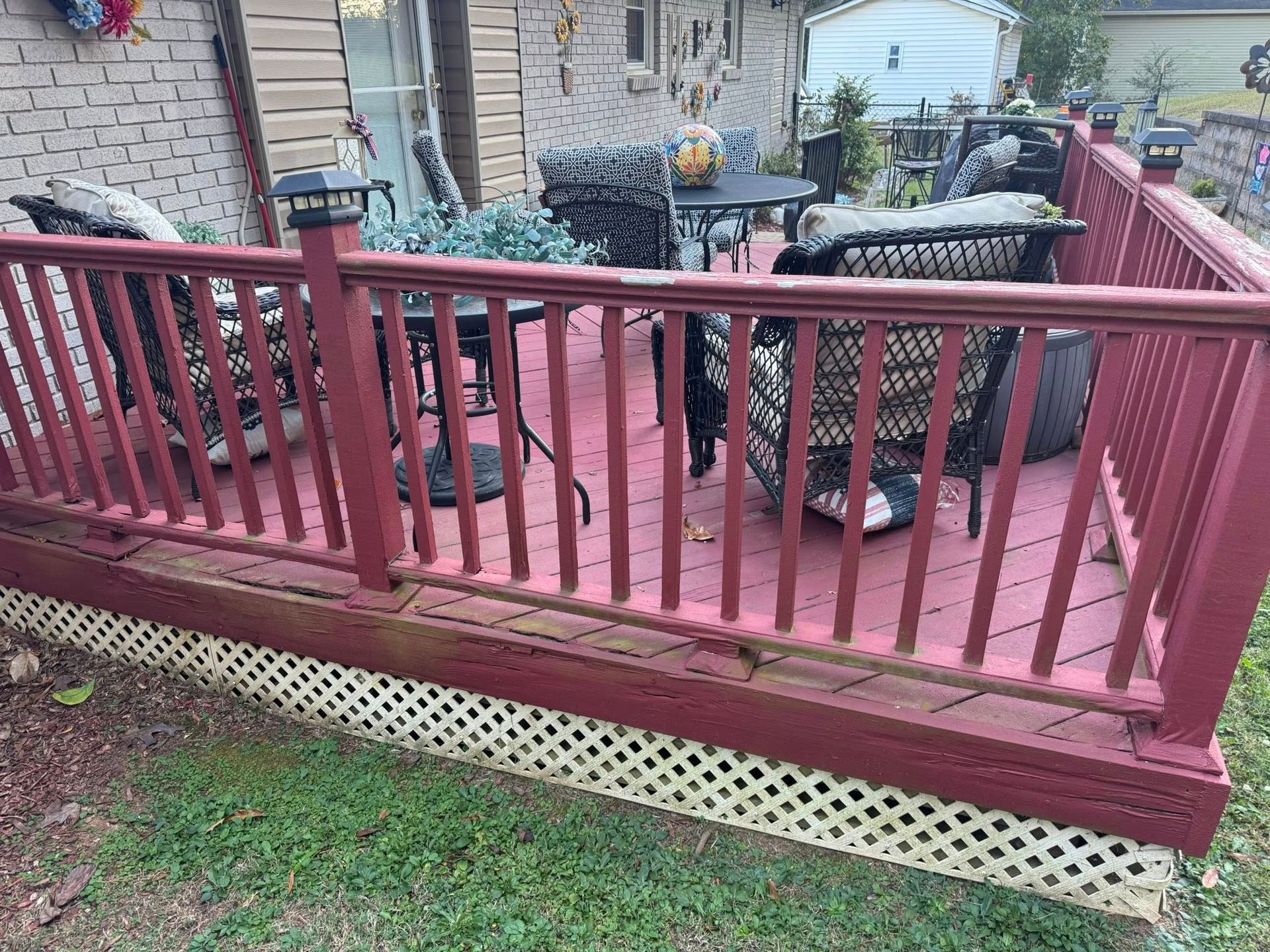 Red-painted wooden deck with wicker furniture and solar lights, in a backyard setting.
