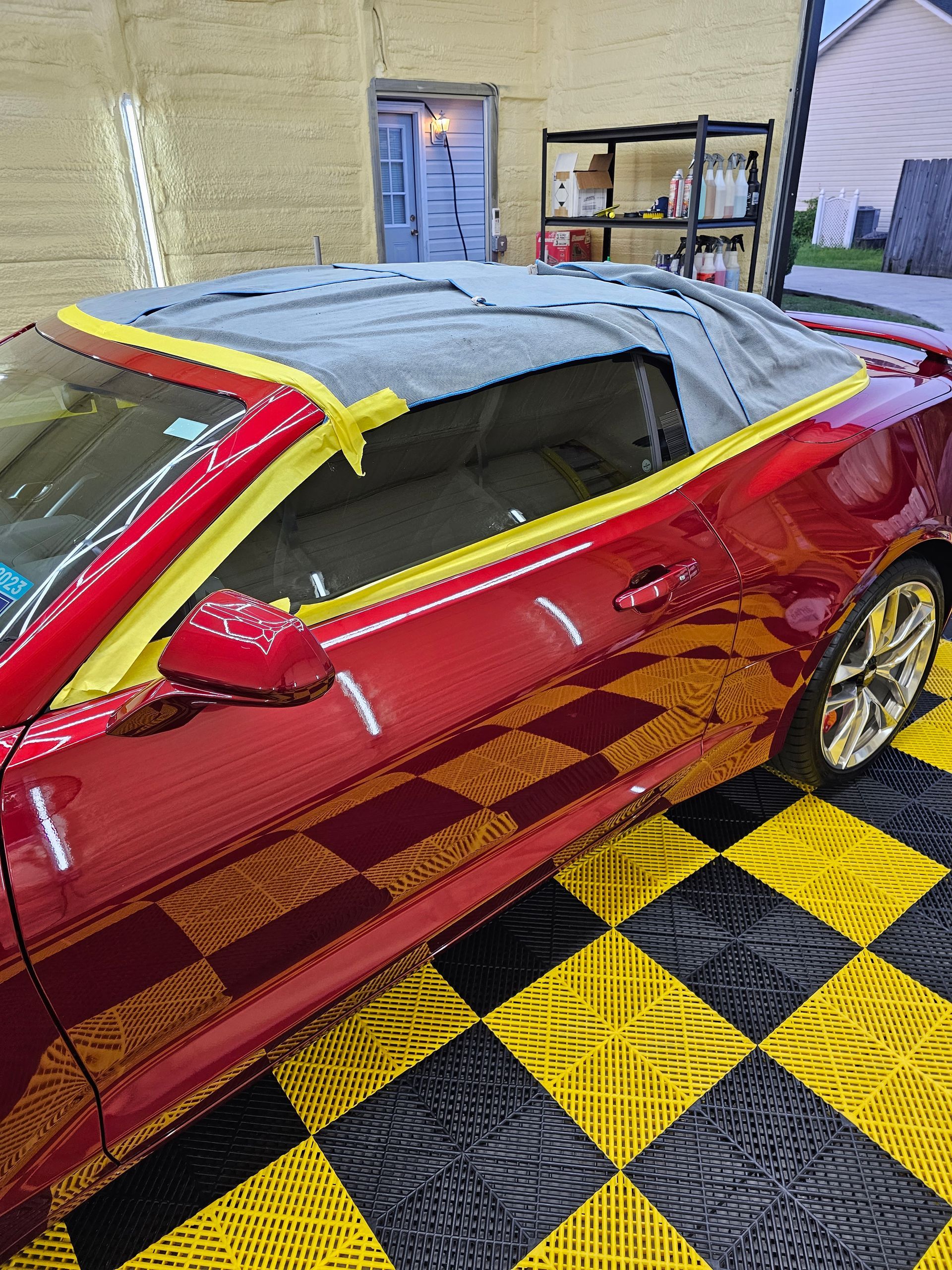 A red convertible car is sitting on a checkered floor in a garage.