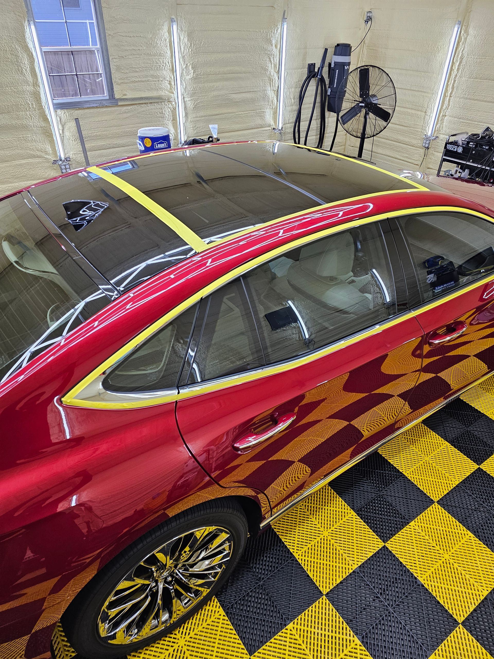 A red car is sitting on a checkered floor in a garage.