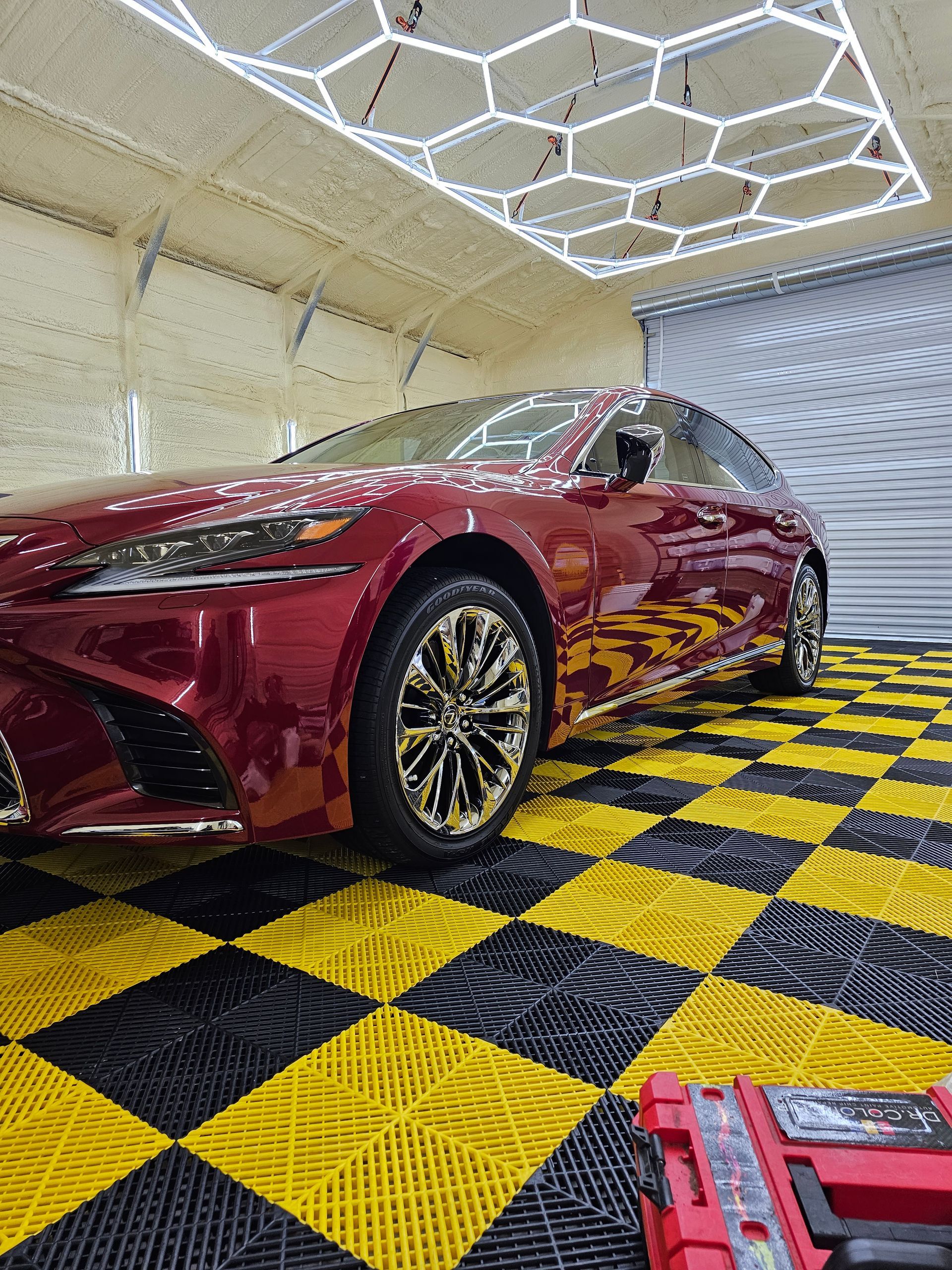 A man is kneeling down next to a car in a garage looking at his phone.