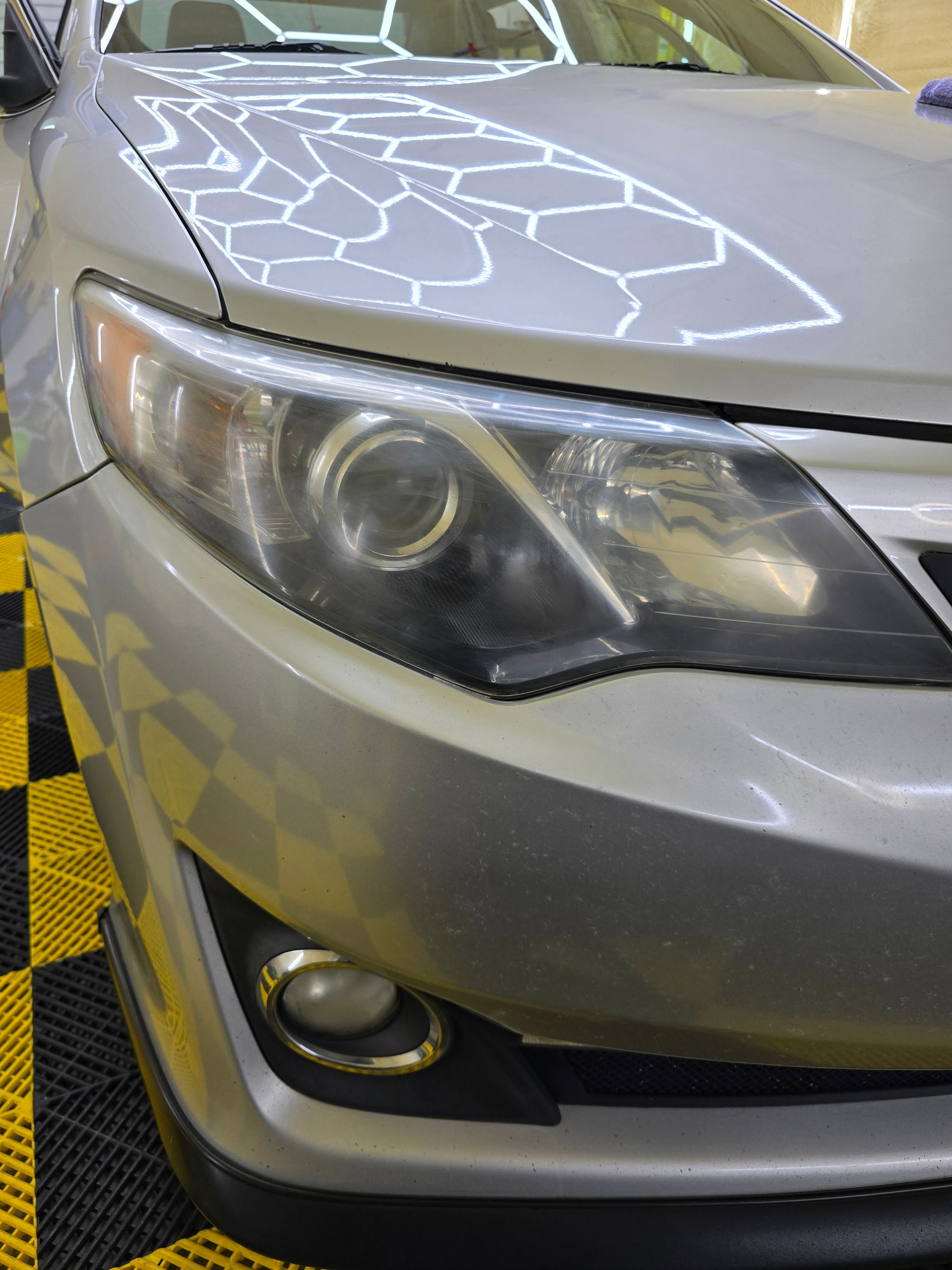 A silver car is parked on a yellow and black checkered floor.