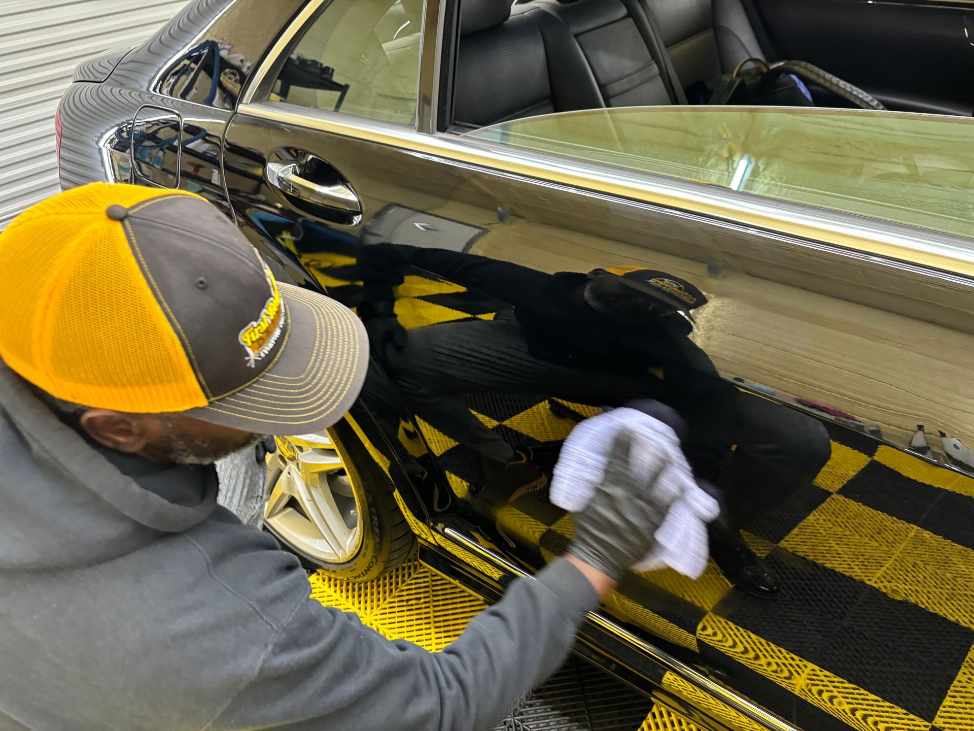 A man in a yellow hat is cleaning a car with a cloth.