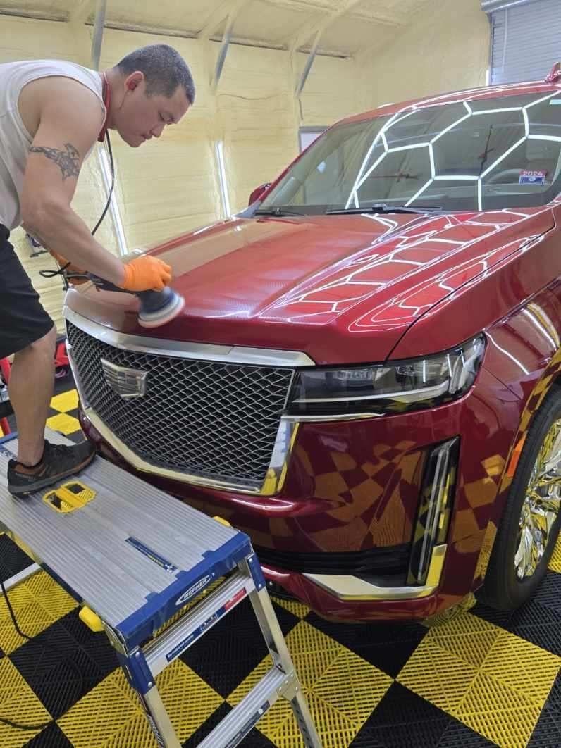 A man is polishing a car with a machine in a garage.