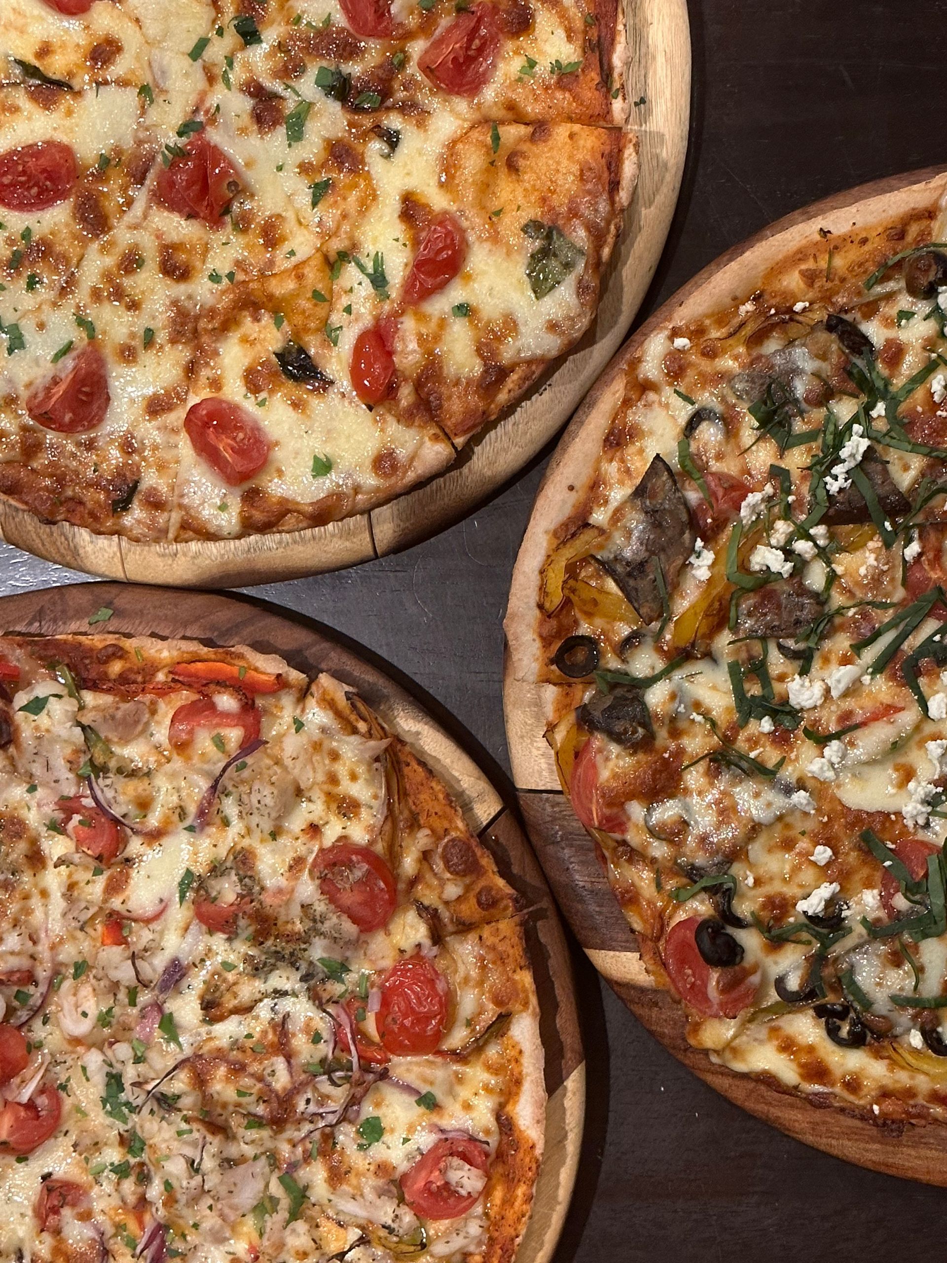 Three pizzas are sitting on a wooden table.