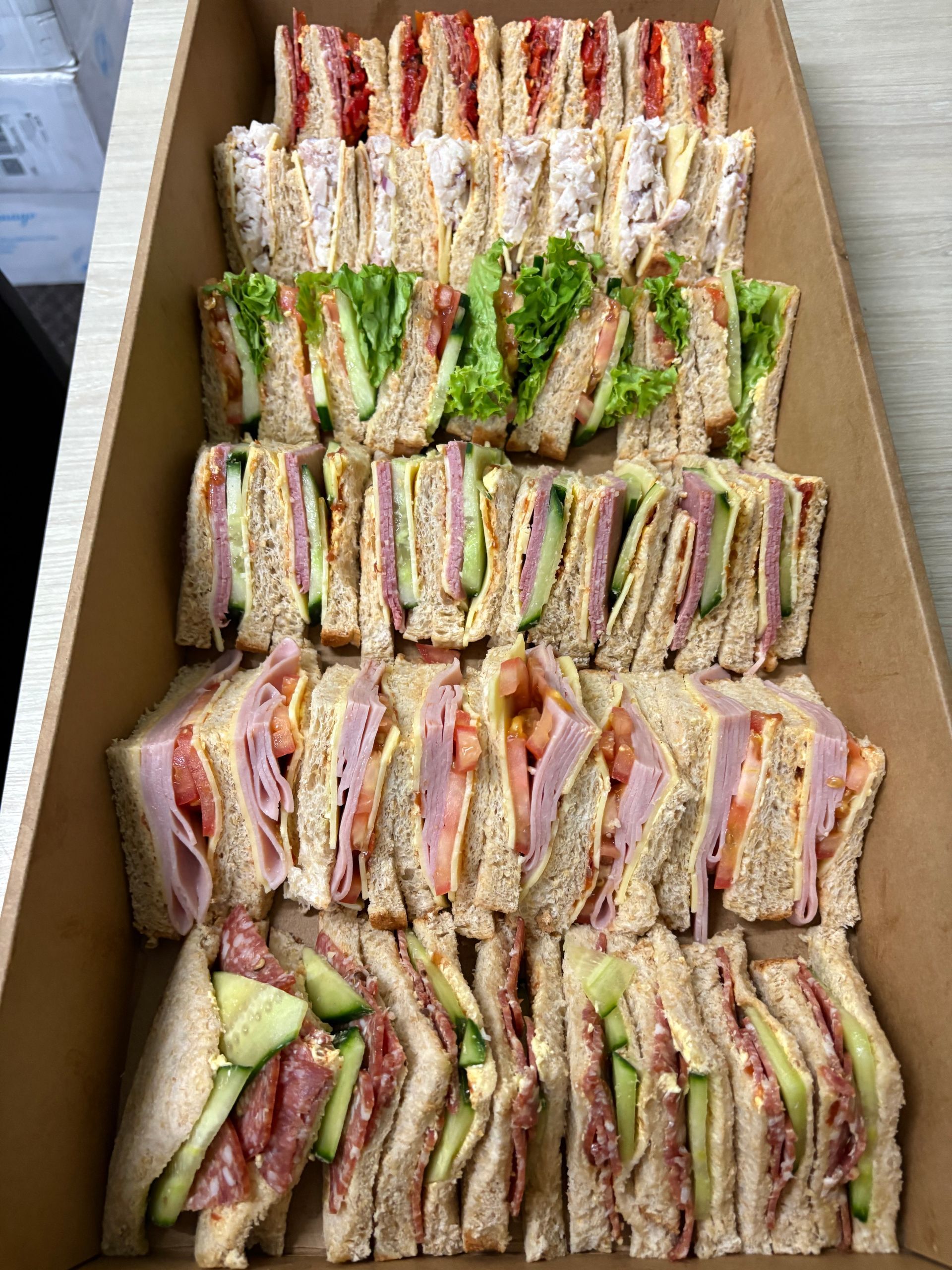 A cardboard box filled with a variety of sandwiches on a table.