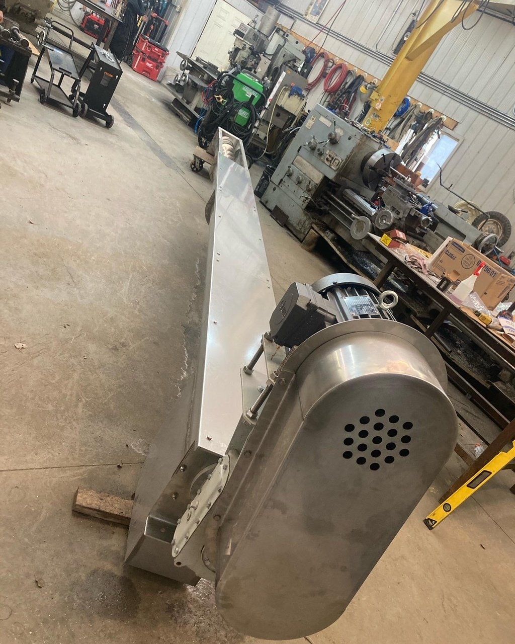 A large stainless steel machine is sitting on the floor in a workshop.