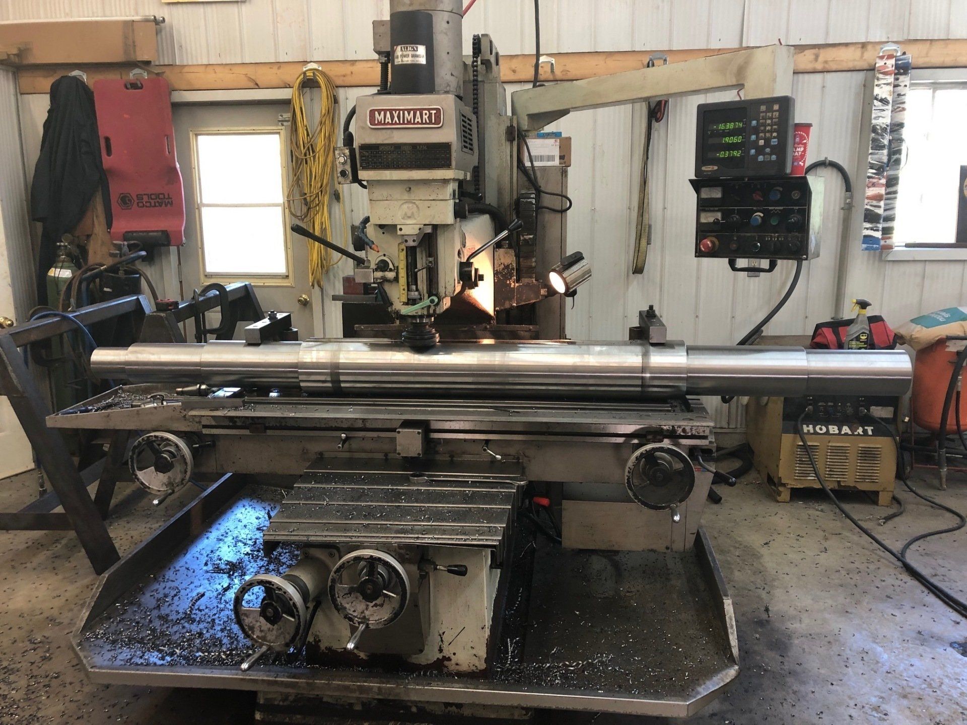 A milling machine is sitting in a garage with a large piece of metal on it.