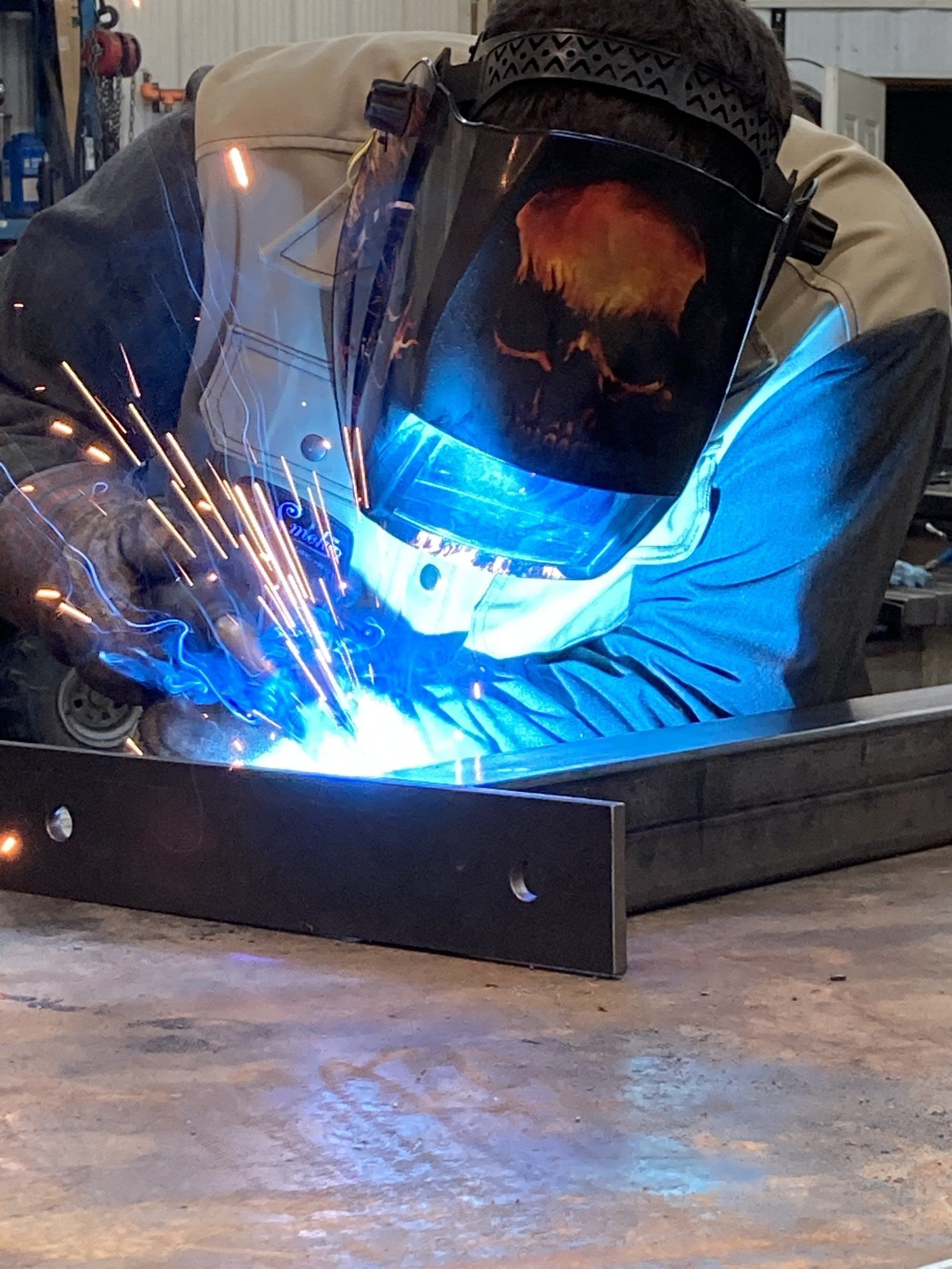 A man wearing a welding mask is welding a piece of metal