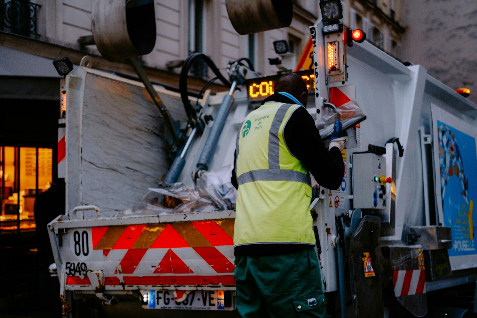 Garbage truck with worker in safety vest; rear view.