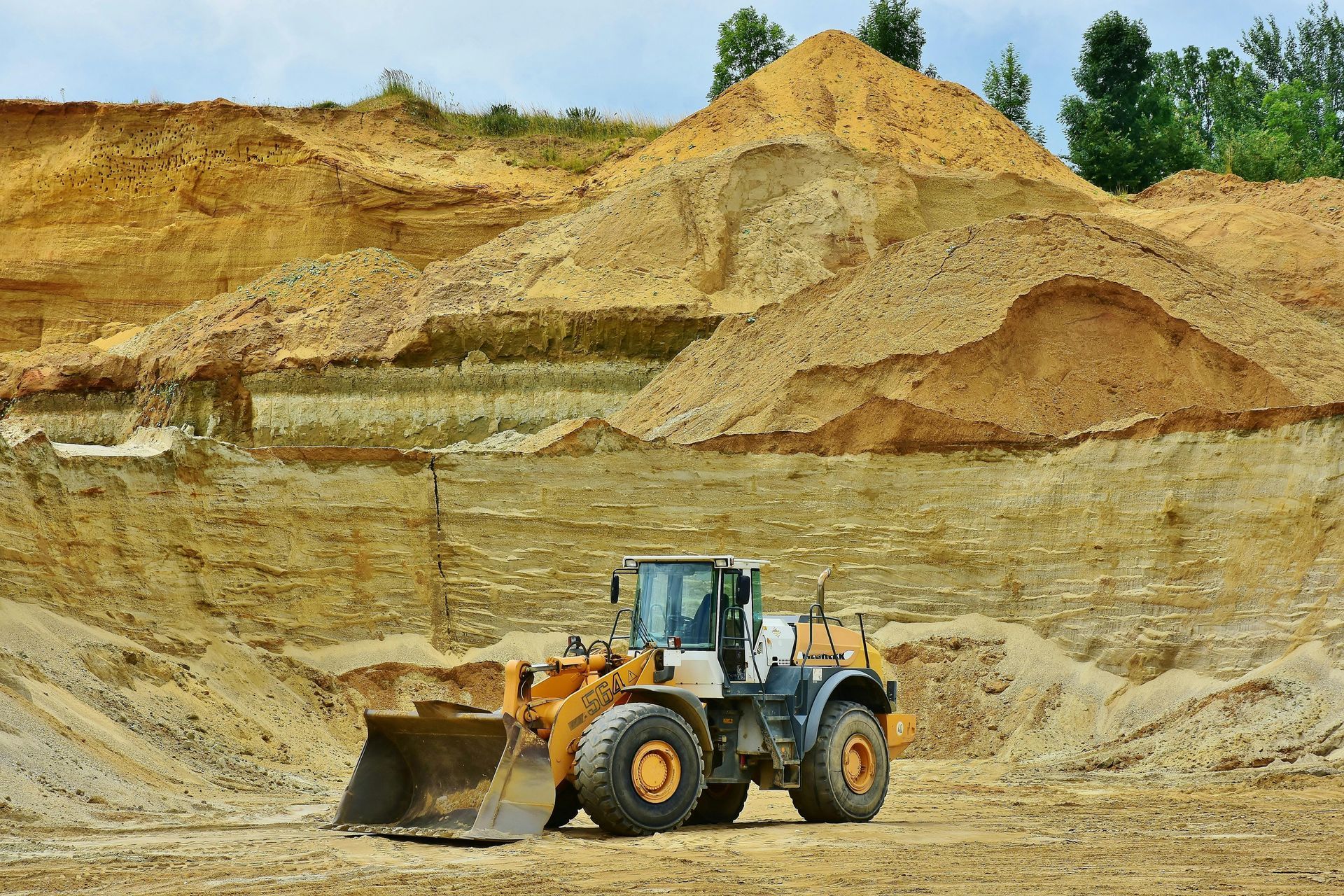 A yellow and grey front-end loader in a sand pit, with piles of sand in the background.