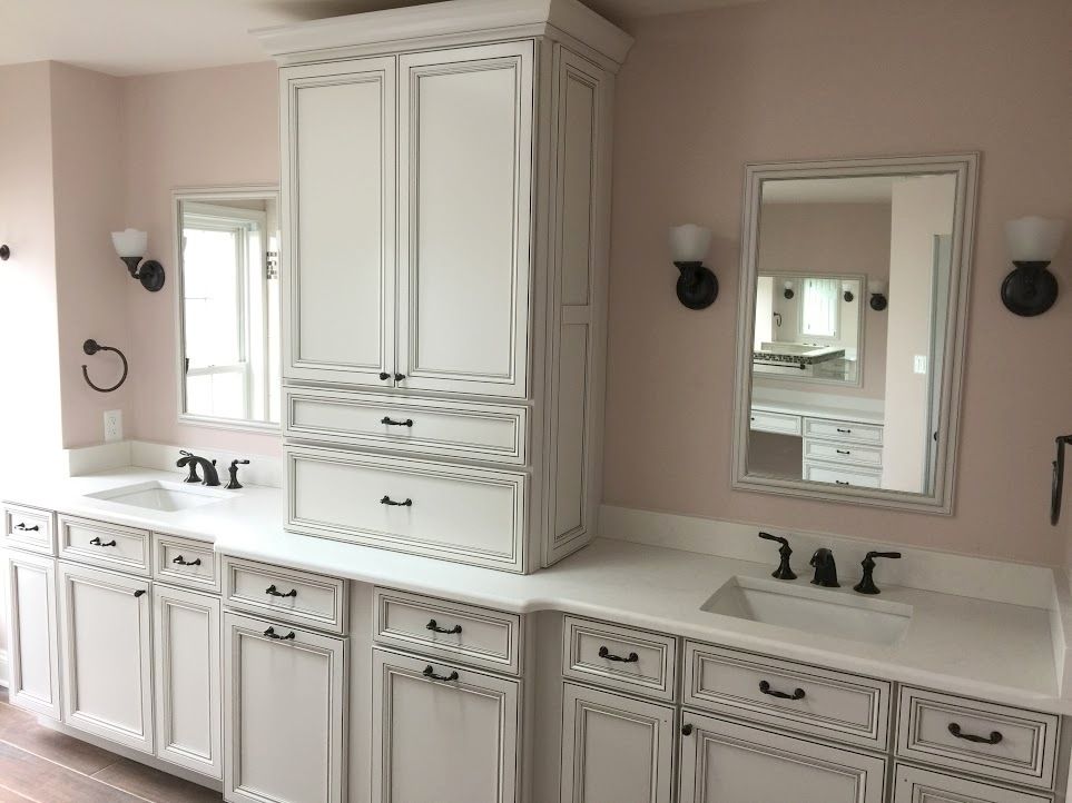 A bathroom with white cabinets , sinks and mirrors.