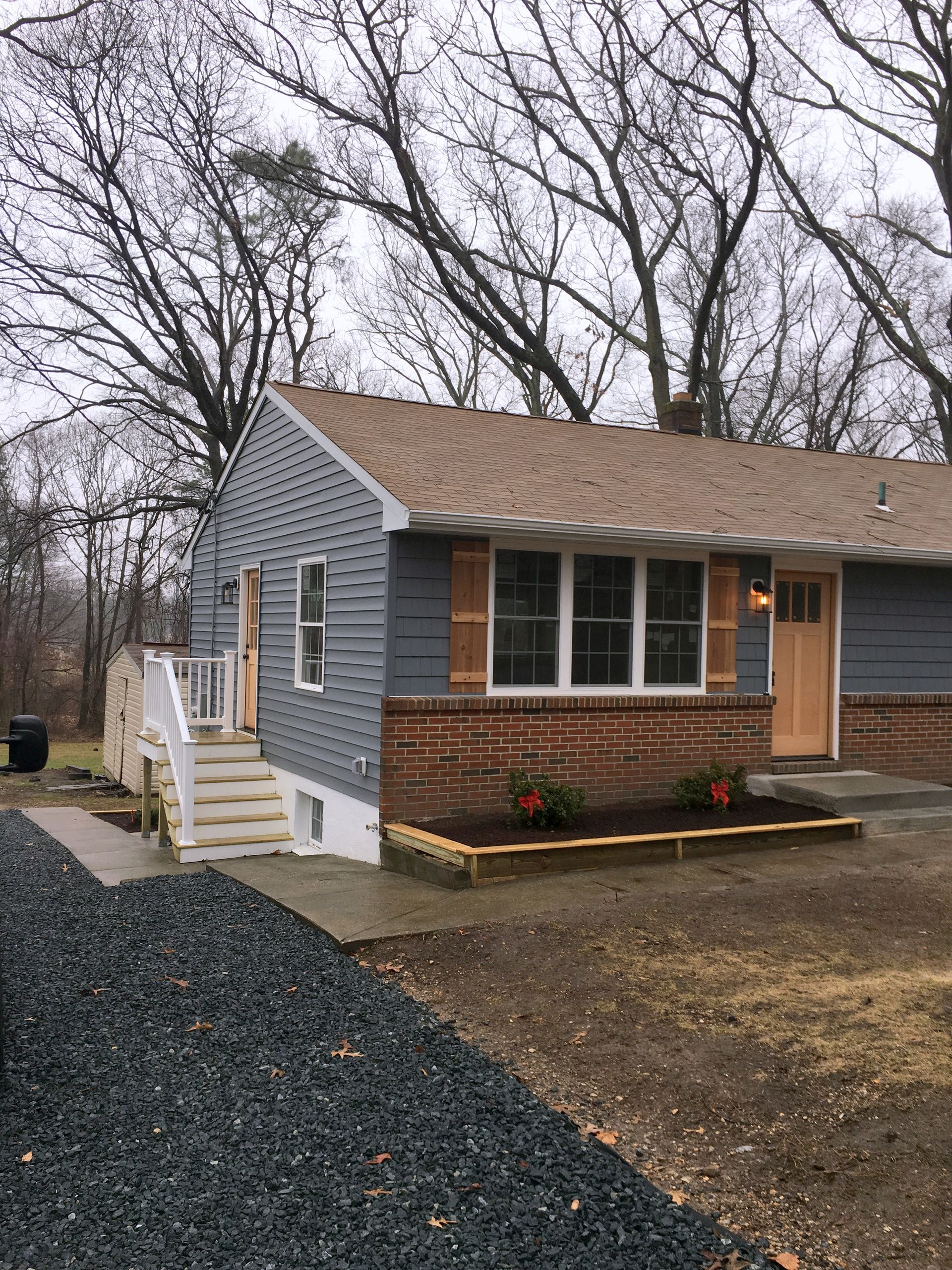 A blue house with a brown roof and a gravel driveway in front of it.