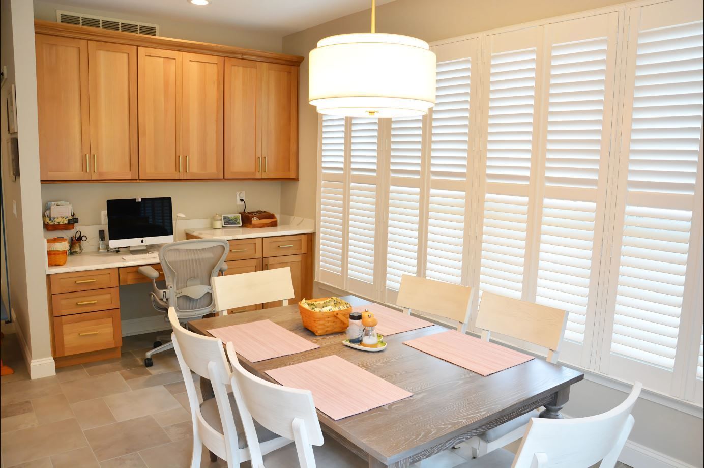 A dining room with a table and chairs and shutters on the windows.