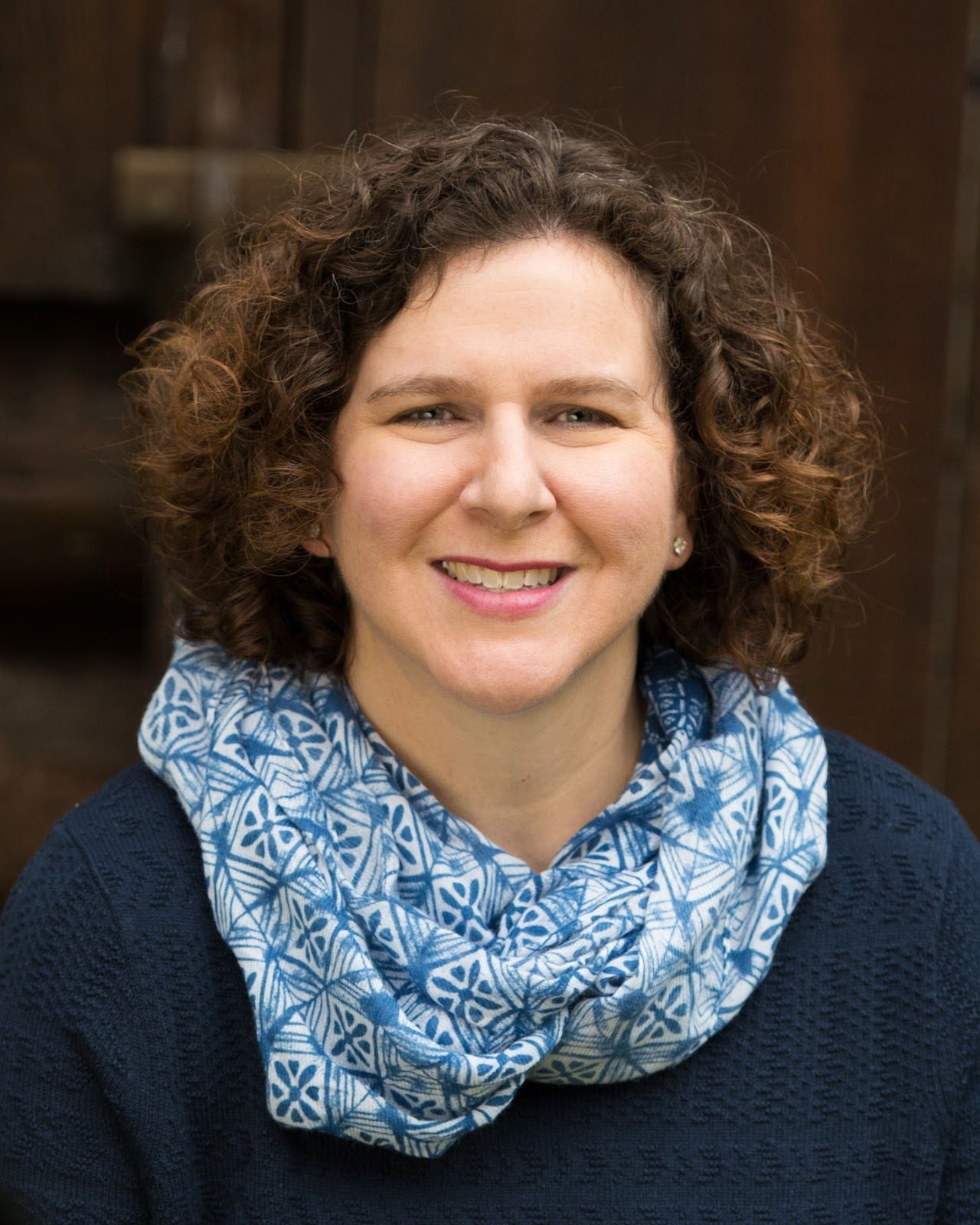 A woman with curly hair is wearing a blue scarf around her neck.